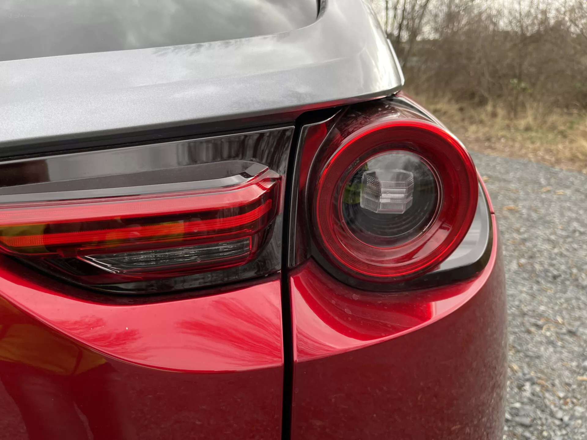 Närbild av bakre hörnet på en Mazda MX-30 2020 som visar detaljerad baklyktdesign, glänsande röd färg och reflektion på dess kaross, vilket framhäver modern fordonsbelystningsteknik och design.