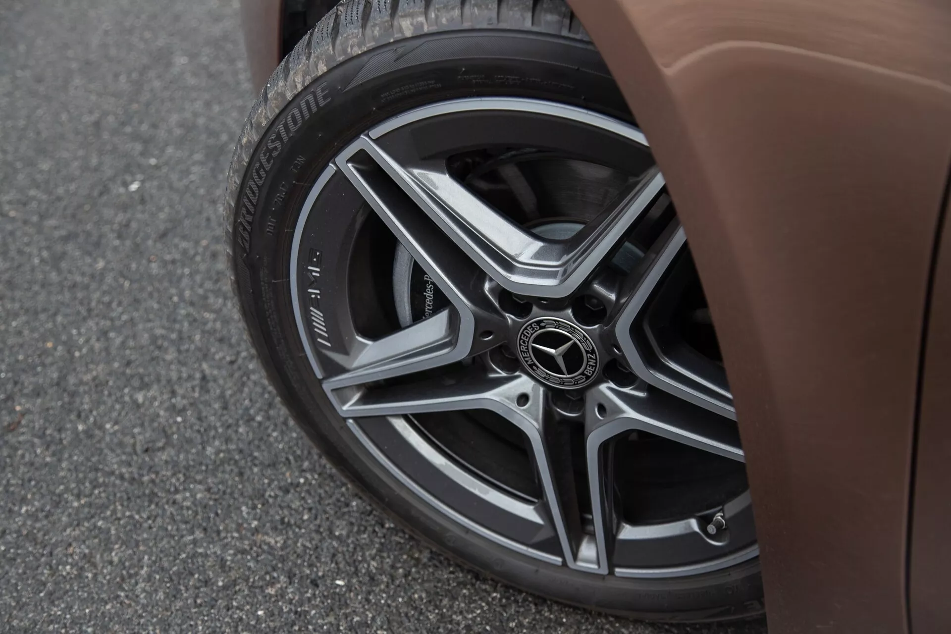 Närbild av den nedre sidodelen av en Mercedes-Benz A-Klasse 2022 som visar ett flerspakat lättmetallhjul med Bridgestone Turanza-däck och en brun karosspanel mot en asfaltsbakgrund