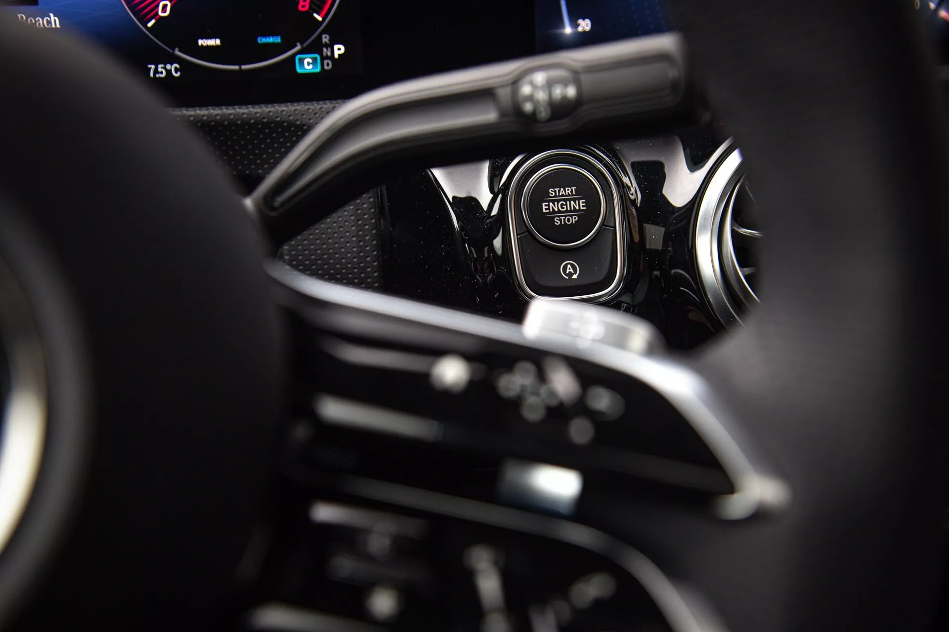 Närbild av start/stopp-knappen i en Mercedes-Benz A-Klass 2022 med kromlist, delvis synligt ratt, paddlar för växling och digitala instrumentbrädans mätare ur förarens perspektiv