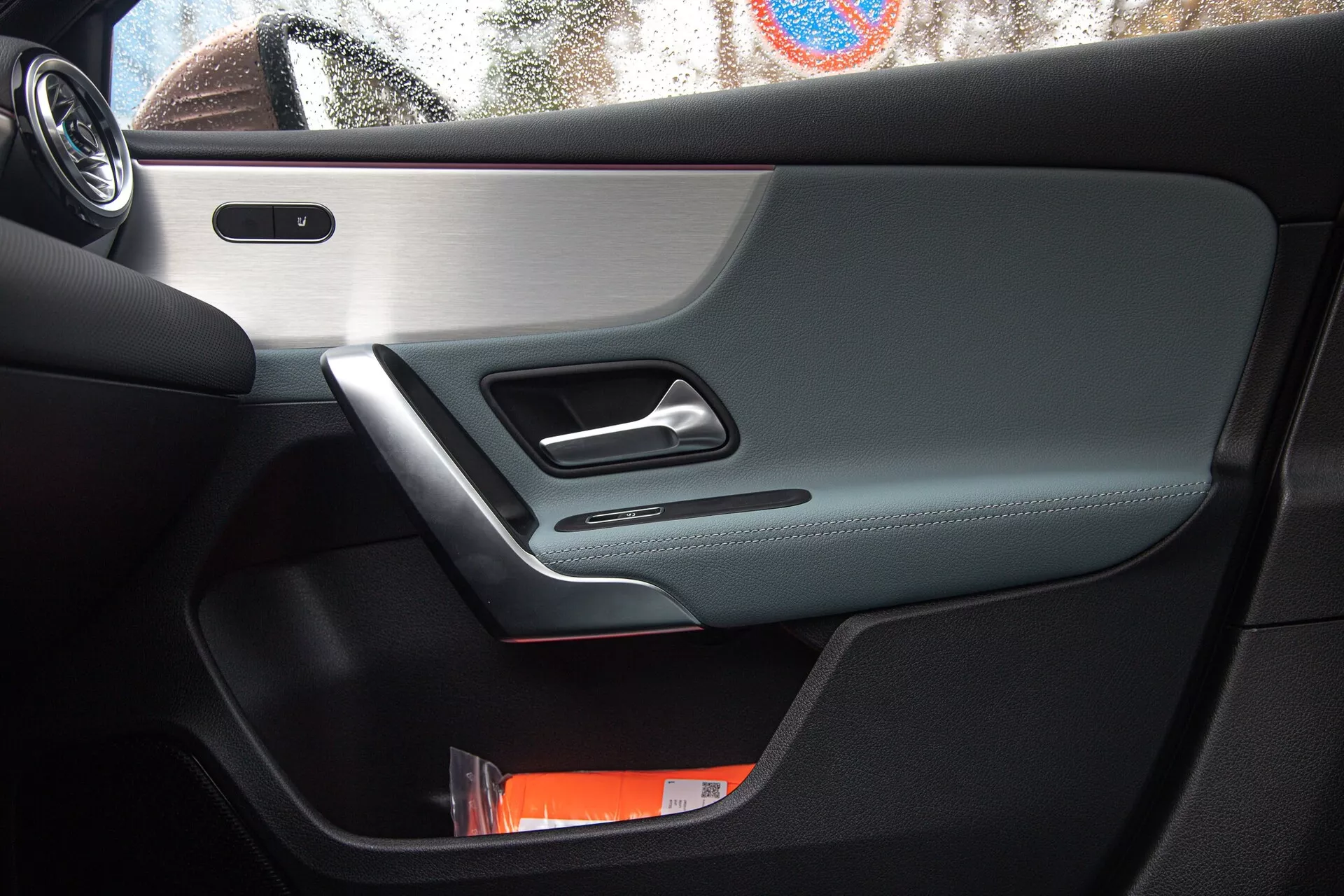 Interiörvy av Mercedes-Benz A-Klass 2022 med fokus på förarens dörr med kromad dörrhandtag, kontrollpanel, inbyggd högtalare, förvaringsfack och en blandning av lyxmaterial under naturligt ljus