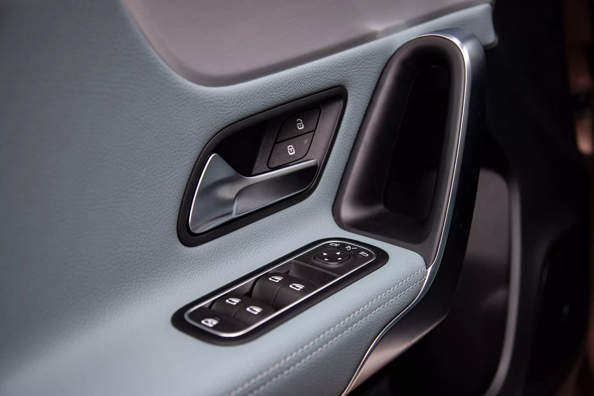 Närbild på interiören i förardörrspanelen i Mercedes-Benz A-klass 2022, som framhäver ergonomisk design och tekniska funktioner såsom spegel- och fönsterkontroller, kromaccentuerat dörrhandtag mot en bakgrund av läderklädsel.