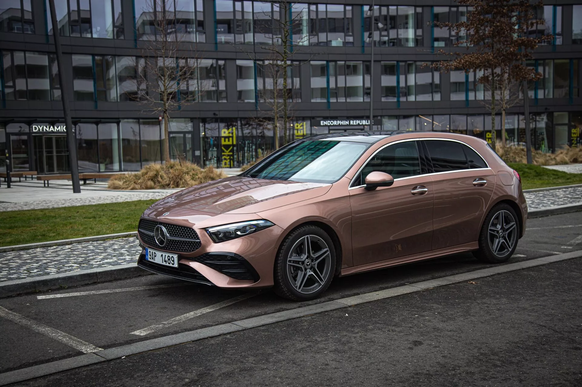 2022 Mercedes-Benz A-klass sedan i en unik metallisk rosaton, sedd från ett trekvartsfrontperspektiv som framhäver dess snygga främre grill, LED-strålkastare, skulpterad huva och flerspakiga lättmetallfälgar mot en urban bakgrund