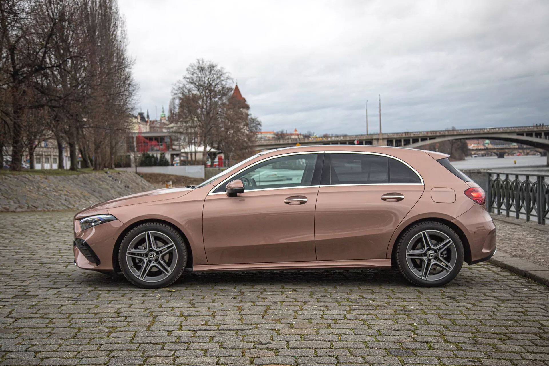 Sidoprofil av 2022 Mercedes-Benz A-Klass hatchback i kopparmetalliskt, med femekrade legeringshjul, nyckelfri entré och aerodynamisk design i en stadsinställning