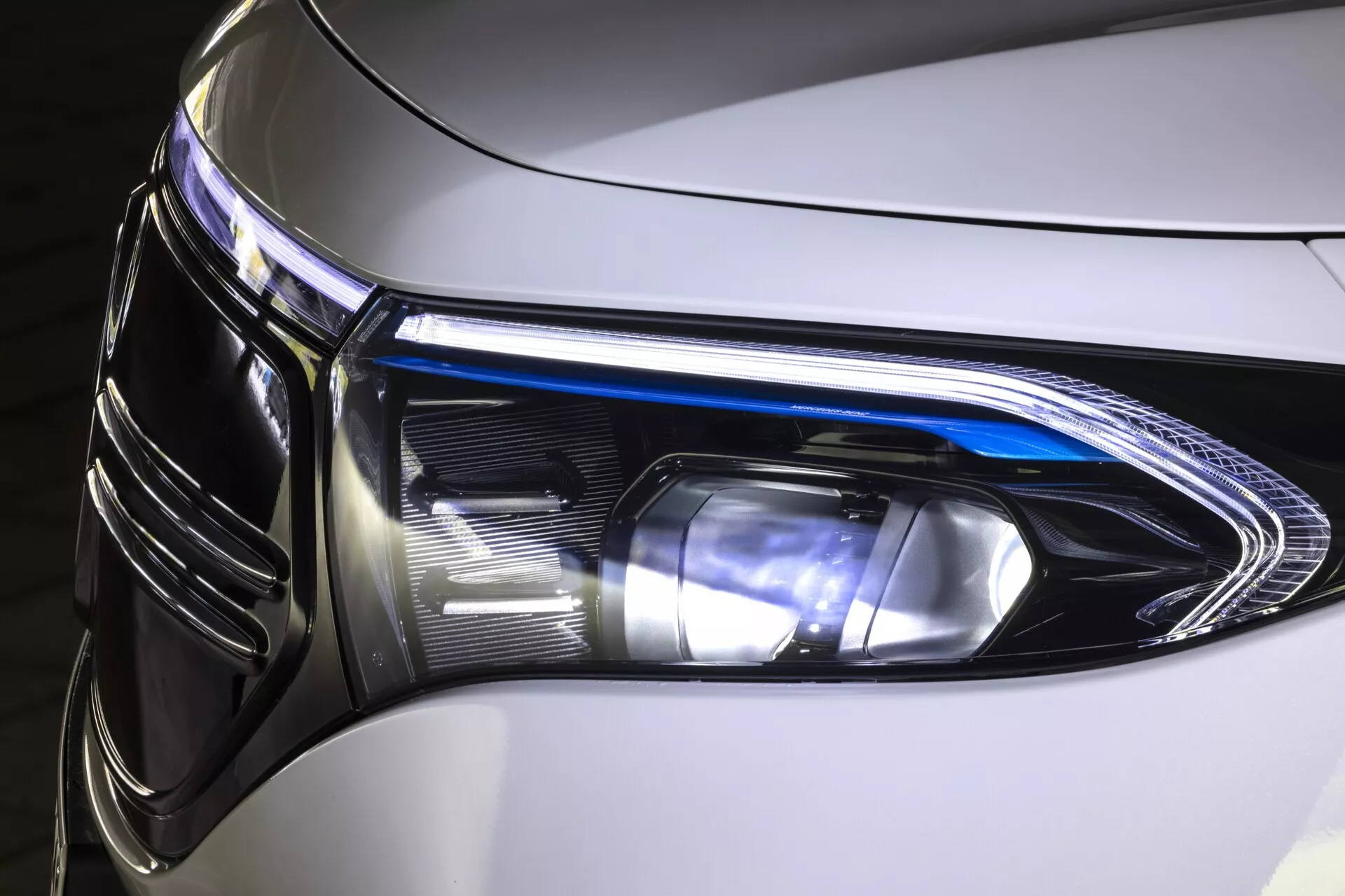 Närbild av strålkastarens sammansättning på 2021 års Mercedes EQB från ett vinklat frontperspektiv, med fokus på vänster sida. Innehåller LED-teknik, dagsljuslyktor, blinkers och funktioner för helljus och halvljus, med ett glänsande svart hölje och en elegant design som är typisk för moderna, lyxiga fordon.