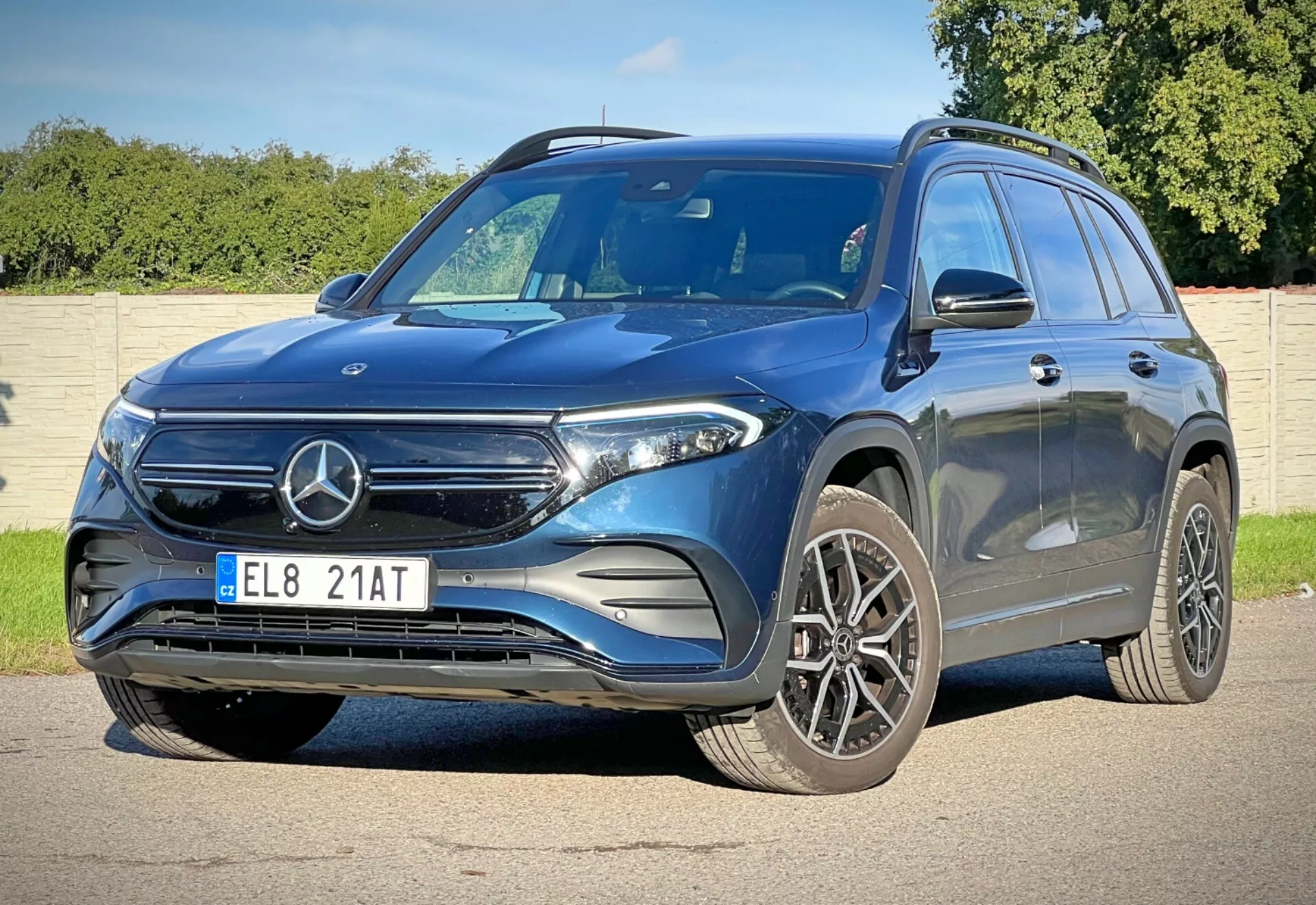 Dynamisk trekvarts framvy av Mercedes-Benz EQB 2021 som visar dess höjd och hållning med funktioner som frontgrill med emblem, LED strålkastare, stora legeringshjul, sportig frontstötfångare, konturerad Motorhuv för aerodynamik, integrerade blinkers i sidespeglarna, en karaktärslinje för en dynamisk look, takräcken för ökad användbarhet och tonade rutor för privatlivet, på en solig dag