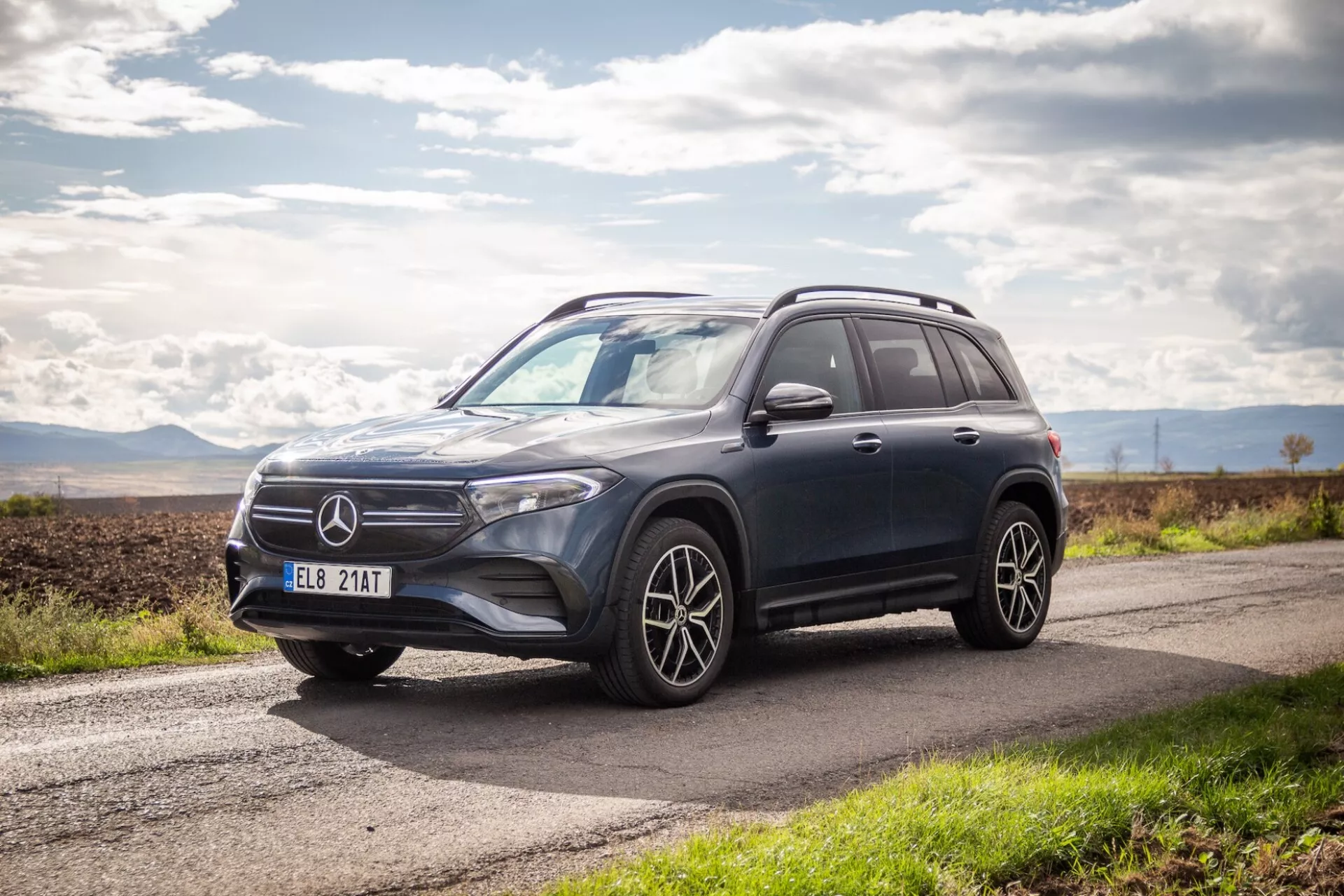 Sidovy och framsida av 2021 års lyxiga SUV Mercedes-Benz EQB som visar aerodynamisk design, LED-strålkastare, flerspakiga lättmetallhjul och hög markfrigång på en asfalterad väg under delvis molnig himmel