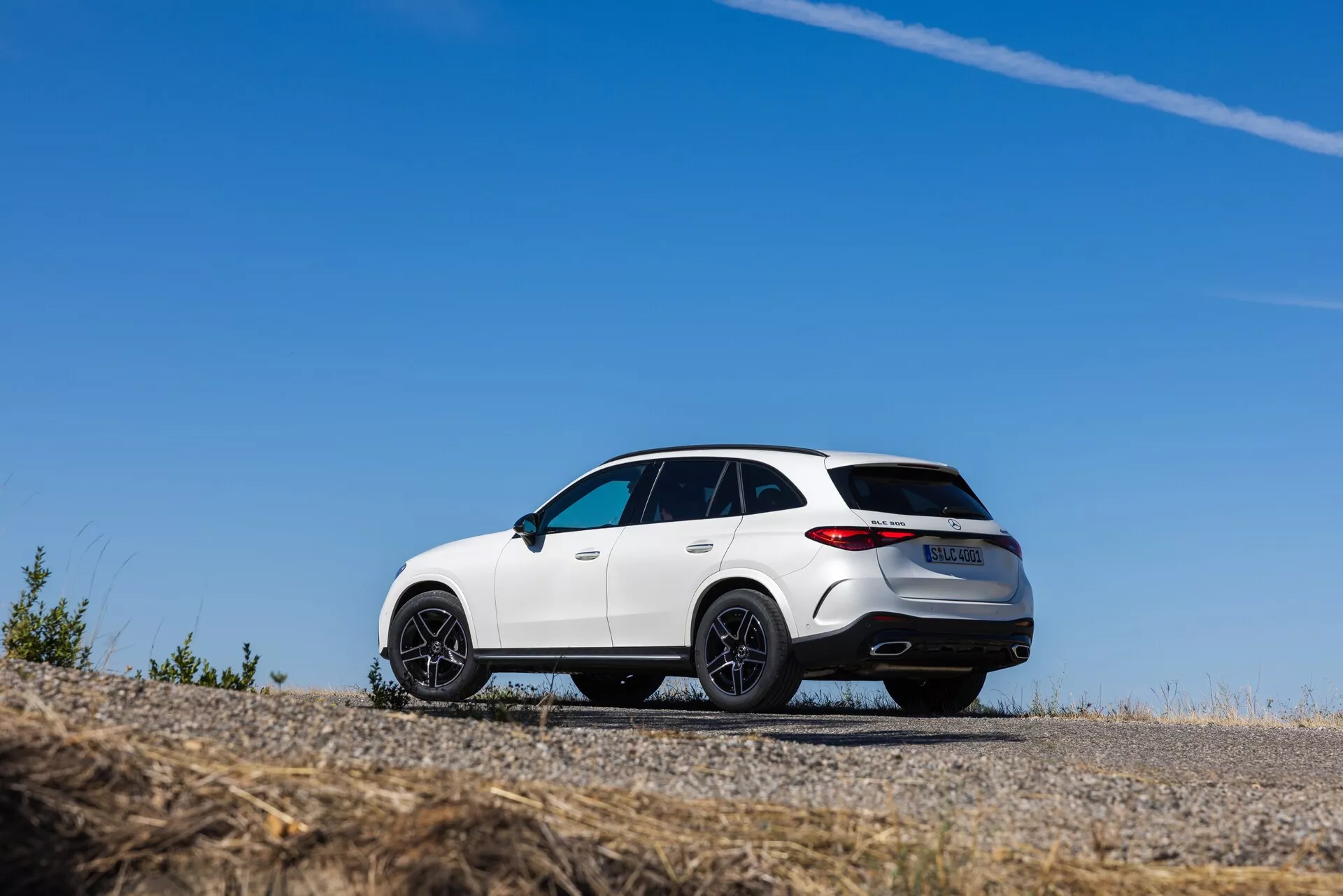 En låg vinkel, trekvarts bakifrånvy av en vit Mercedes GLC 2022 SUV, parkerad på en asfalterad yta, som visar upp dess sportiga design med en sluttande taklinje, stora svarta fler-ekrade lättmetallfälgar och LED-bakljus. Bilen har kromade detaljer, dubbla avgasrör, en bakspoiler, panoramasoltak och en bakre diffusor, vilket betonar dess premiumkonstruktion och prestandaattraktion.
