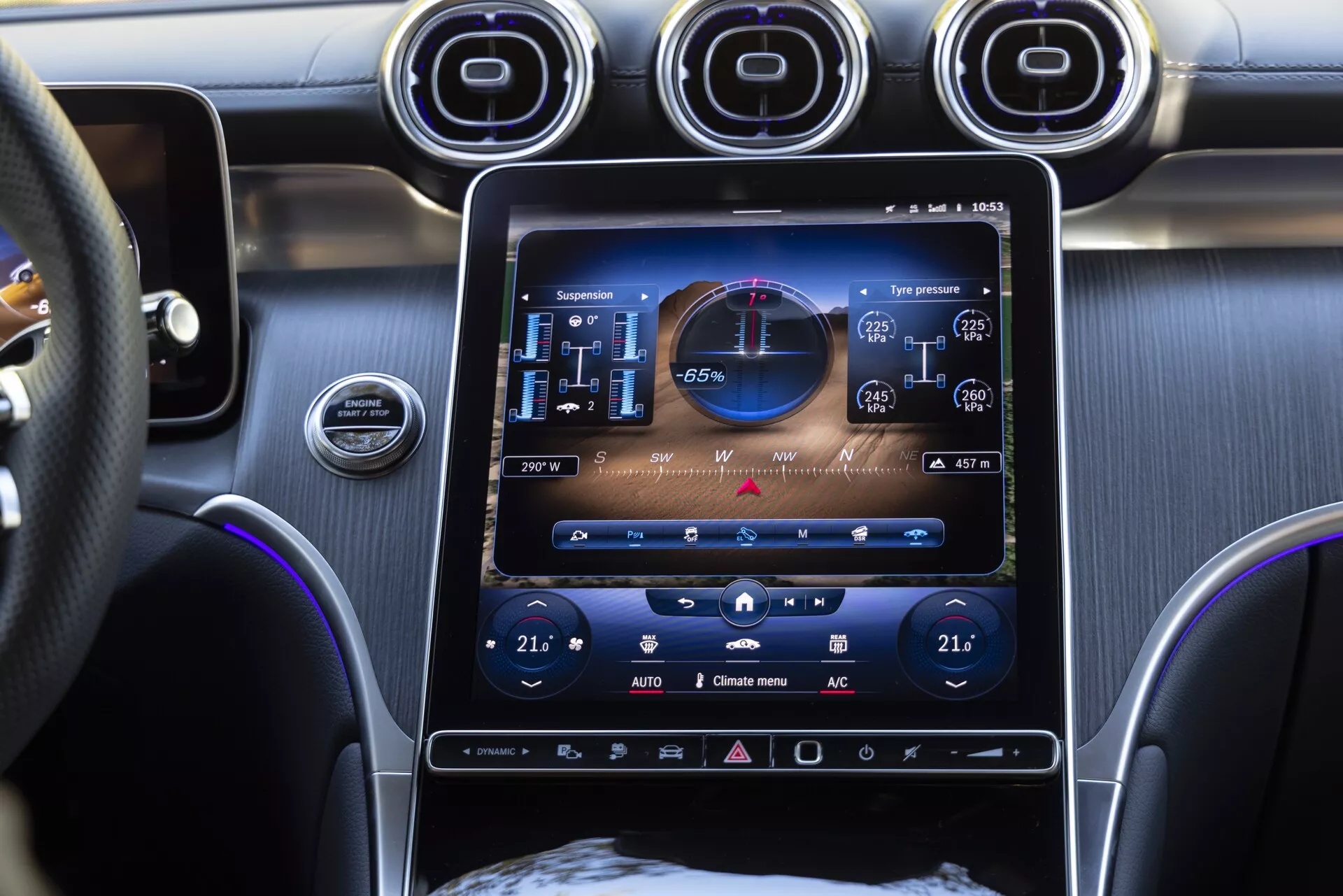 Interiörvy av en Mercedes GLC 2022 med fokus på den centrala infotainmentsystemet och instrumentbrädan, visar en stor pekskärm med högupplöst grafik, inklusive en GPS-navigeringskarta, information om däcktryck och en eco-driving-indikator. Under skärmen finns dubbelzons klimatanläggning kontroller, och ovanför skärmen finns tre cirkulära luftventiler med metallisk finish. Bilden, tagen ur passagerarens perspektiv, visar även en del av ratten och antyder på användningen av premiummaterial i interiören, som borstad metall och läder.