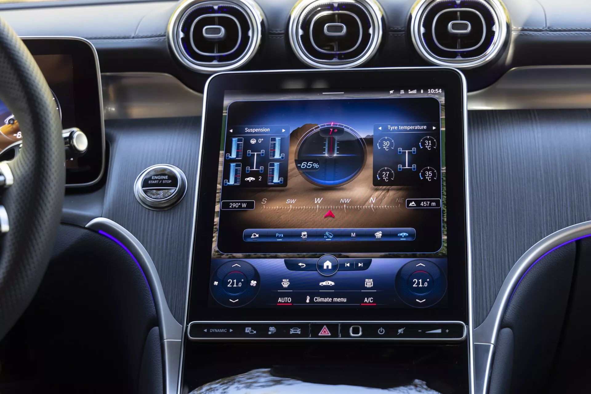 Närbild av den centrala konsolen i Mercedes GLC 2022 med ett vertikalt monterat, 10-12 tum stort pekskärms infotainmentsystem som visar fordonsstatus med digital hastighetsmätare, varvräknare och klimatkontroller som visar 21 grader Celsius för både passagerare och förare. Den lyxiga interiören inkluderar luftventiler med kromaccent, start/stopp-knapp för motorn, multifunktionell läderklädd ratt och blå omgivande belysning.