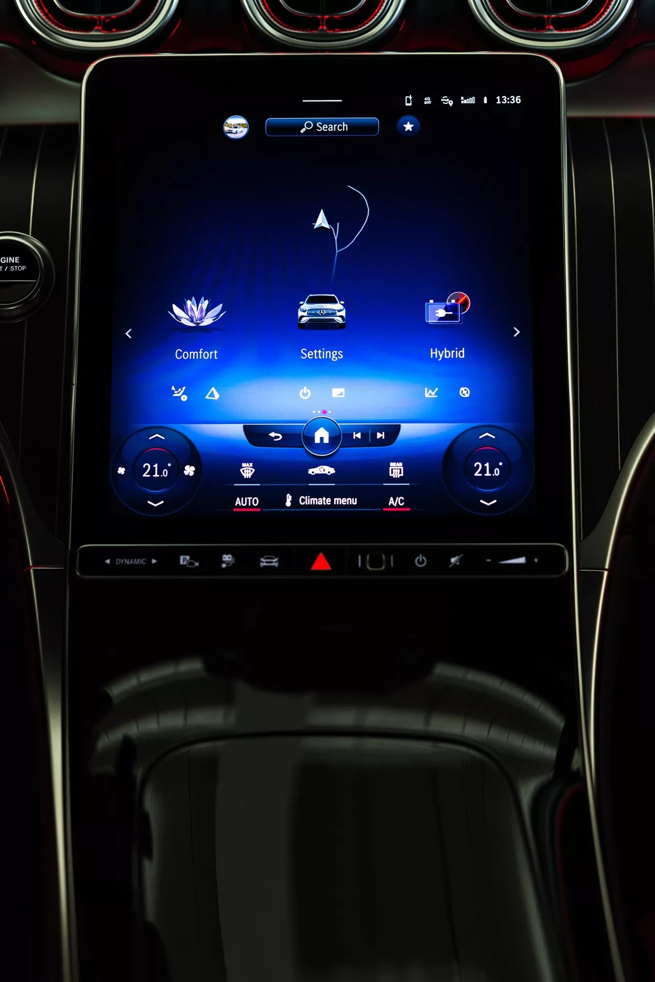 Bilden visar interiören av en 2022 Mercedes GLC, med fokus på den centrala vertikalt orienterade infotainment-pekskärmen på instrumentbrädan. Skärmen visar menyer för 'Comfort,' 'Settings' och 'Hybrid,' som indikerar justerbara komfortfunktioner och en hybrid-drivlina. Klimatkontroller för dubbla zoner är inställda på 21 grader Celsius. Omgivningen inkluderar cirkulära luftventiler med metallfinish, vilket ger en lyxig design. Fotot är taget från förarens perspektiv och betonar avancerade teknologiska och anslutningsfunktioner.