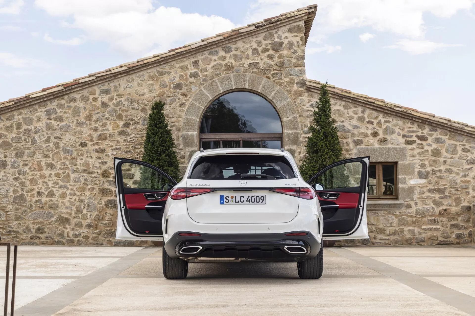 Bakifrånvy av en stillastående 2022 Mercedes GLC med öppen bagagelucka och bakdörrar på glänt, visar dubbla avgasrör, eleganta LED-bakljus, monterad registreringsskylt, modellmärke och praktisk plan lastyta med bakre dörrpaneler i kontrasterande färgschema och metalliska trim.