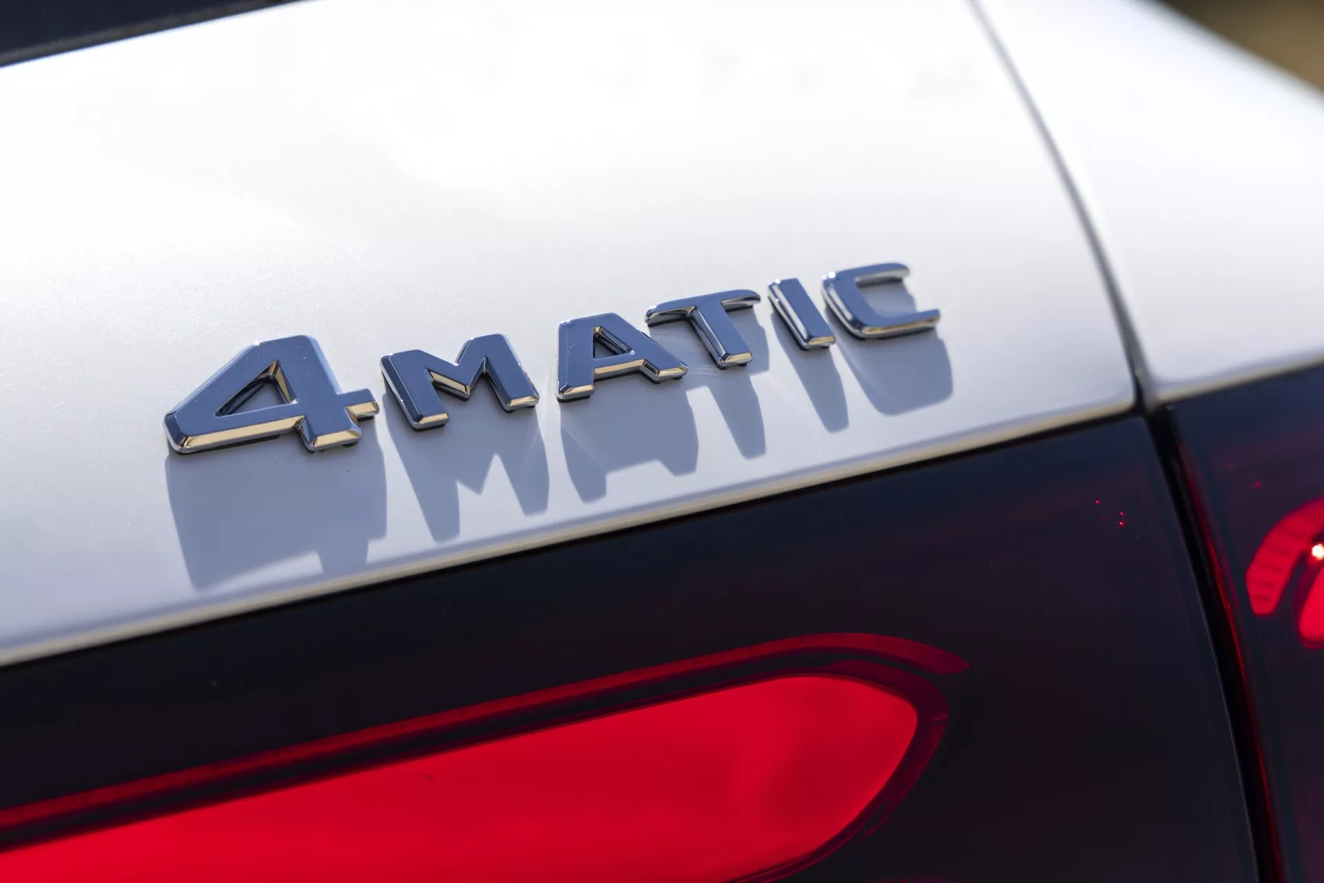 Närbild av 4MATIC-märket på baksidan av en Mercedes GLC 2022. Fotografiet fångar märket i skarp fokus med metalliska bokstäver som reflekterar ljus, monterat strax ovanför bakljuset. Bakgrunden är oskarp, vilket framhäver märkets tredimensionella effekt och kontrasten mot bilens mörka lack. Baklyktans design delvis synlig i nedre högra hörnet.