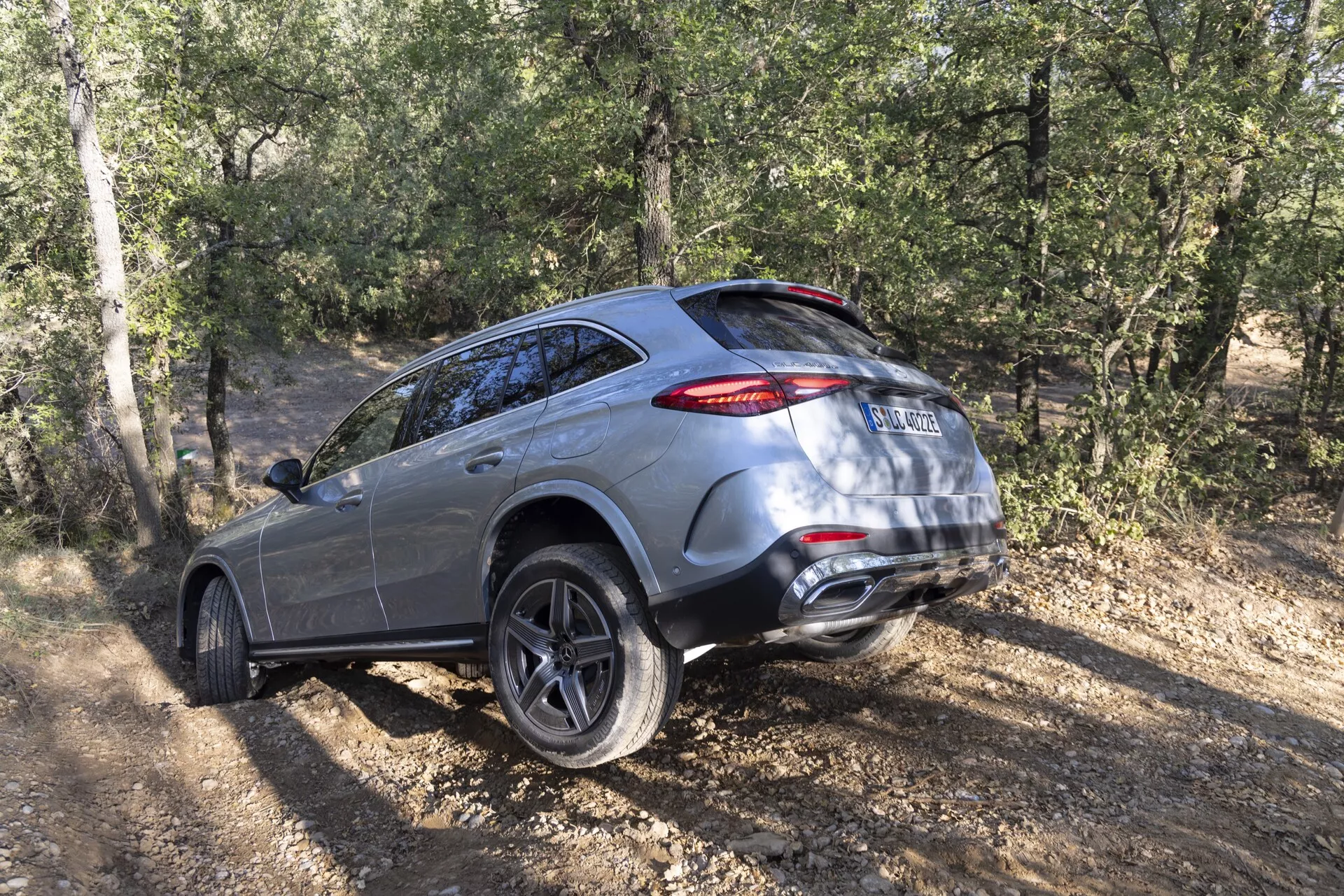 Bakre trekvartsvy av en Mercedes GLC SUV 2022 på oasfalterad mark, som visar sina lyx- och moderndesignfunktioner såsom fler-ekrade lättmetallfälgar, LED-bakljus, dubbla avgasrör och terrängkapabiliteter med bladverk och träd i bakgrunden.