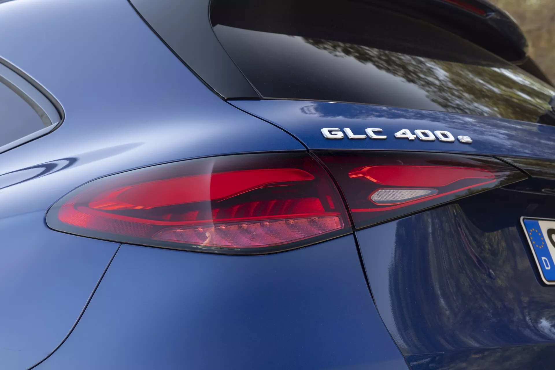 Närbild, vinklad vy av bakdelen på en Mercedes-Benz GLC 400 modell 2022. Fokus är på modellbeteckningen 'GLC 400' och en del av en modern LED-baklyktessamling. Fotot framhäver bilens kurviga kropp, den släta metalliska blå lacken och den eleganta designen på de bakre elementen, inklusive de röda och klara linsdelarna av baklyktan. Den kromade finishen på 'GLC 400'-emblemet antyder specifikationer för prestanda- och drivteknologi.