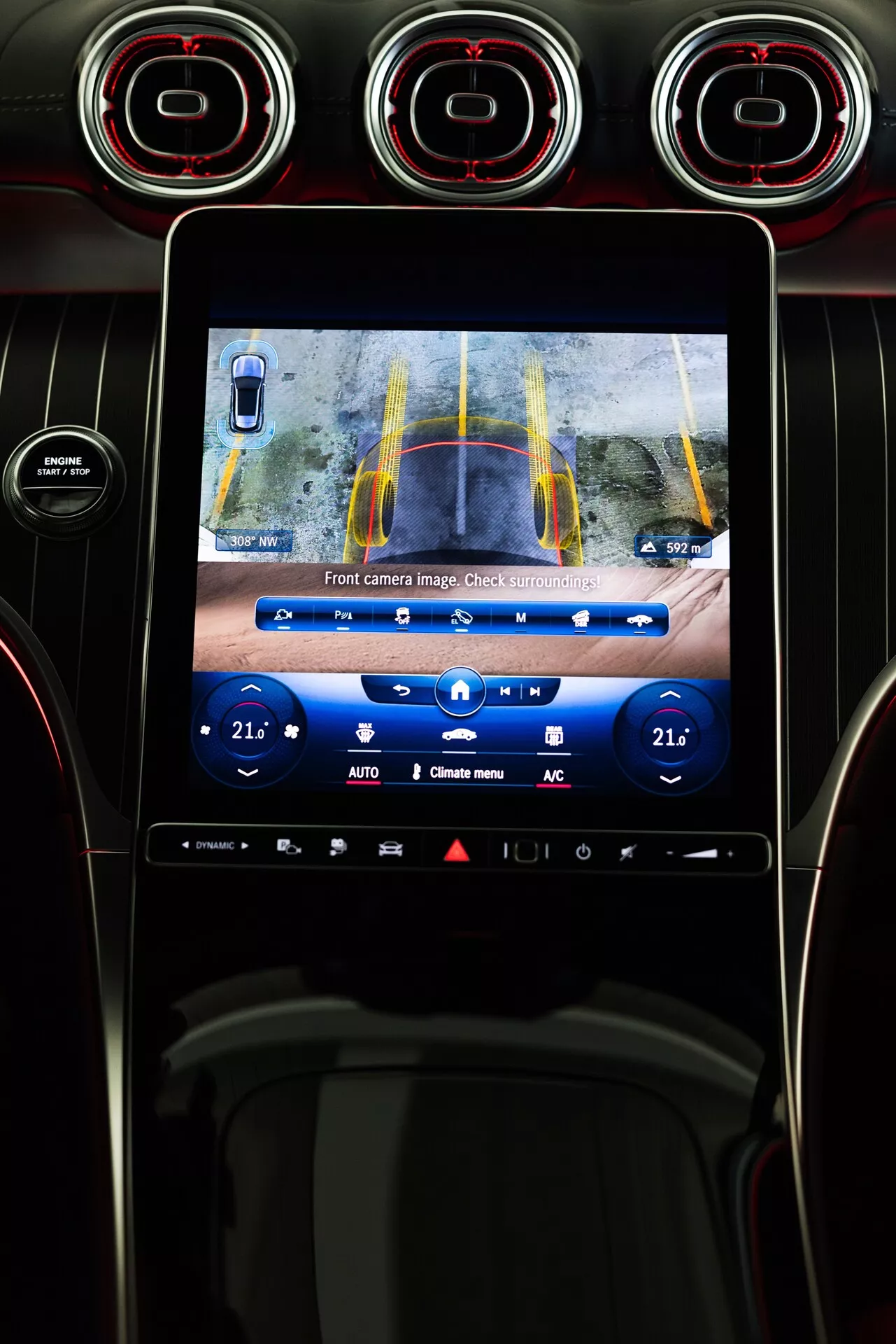 Interiör av 2022 Mercedes GLC med central konsol och infotainment pekskärm som visar bild från framåtvänd kamera med gula och blå riktlinjer för parkeringsassistans. Vy från förarsätet inkluderar ventilationsöppningar med röda detaljer ovan skärmen och klimatkontrollsknappar nedan.