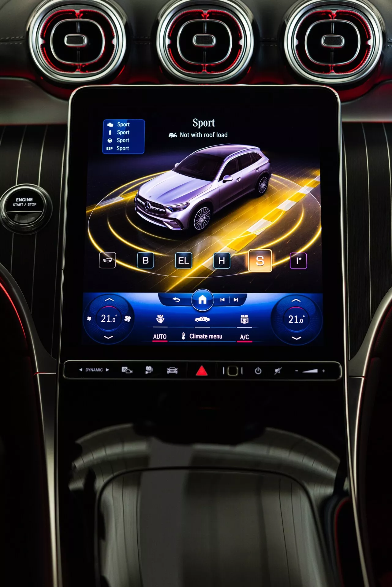 Mercedes GLC 2022 centralkonsol med infotainmentsystem som visar en animerad profilvy av en mörklila bil omgiven av dynamiska gula linjer, i 'Sport' läge med en ikon av en rutad flagga. Pekskärmen är inramad av cirkulära ventilationer med metallfinish och röda accenter. Nedanför skärmen finns touch-känsliga klimatkontroller som visar dubbla zon-temperaturer inställda på 21°C, med ikoner för sätesvärme, klimatkontroll och avfrostning. Blankt svart panel med fler touch-känsliga knappar syns längre ner. Stilen antyder avancerad teknologi och en sportig estetik.