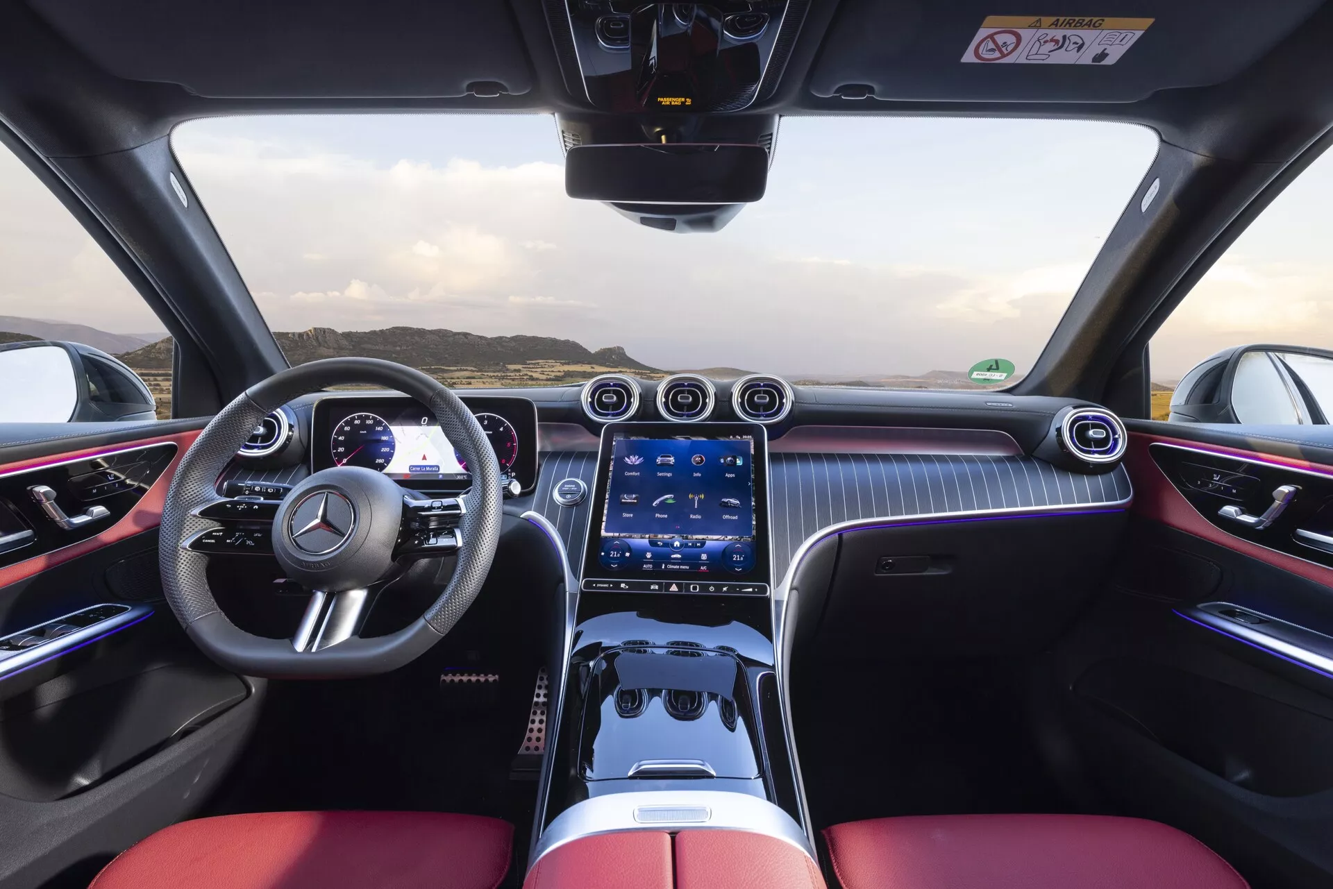 Interiörvy av 2022 Mercedes-Benz GLC 254 från en förarperspektiv som visar sportig ratt med multifunktioner, tvåfärgad cockpit med svarta och klarröda lyxsäten, digital instrumentpanel, bred pekskärmsinfotainmentsystem, kromade luftventiler, fysiska knappar för klimatkontroll, kolfiberliknande mönster, ambient belysning, pekplattakontroll och en högklassig, prestandaorienterad design.
