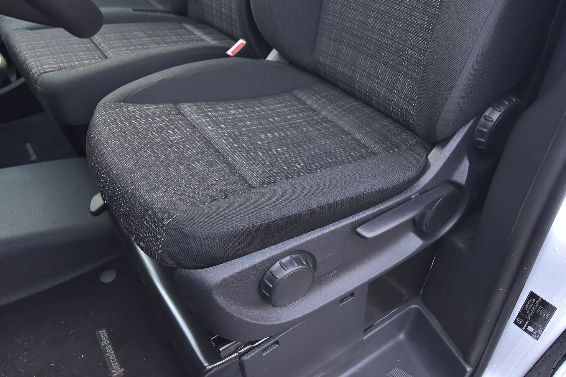 Interiören i Mercedes-Benz Vito 2014 Tourer med fokus på passagerarsätet med hållbart mörkt tygklädsel, knapp för manuell justering och säkerhetsfunktioner som tydligt synlig säkerhetsbältesmottagare.