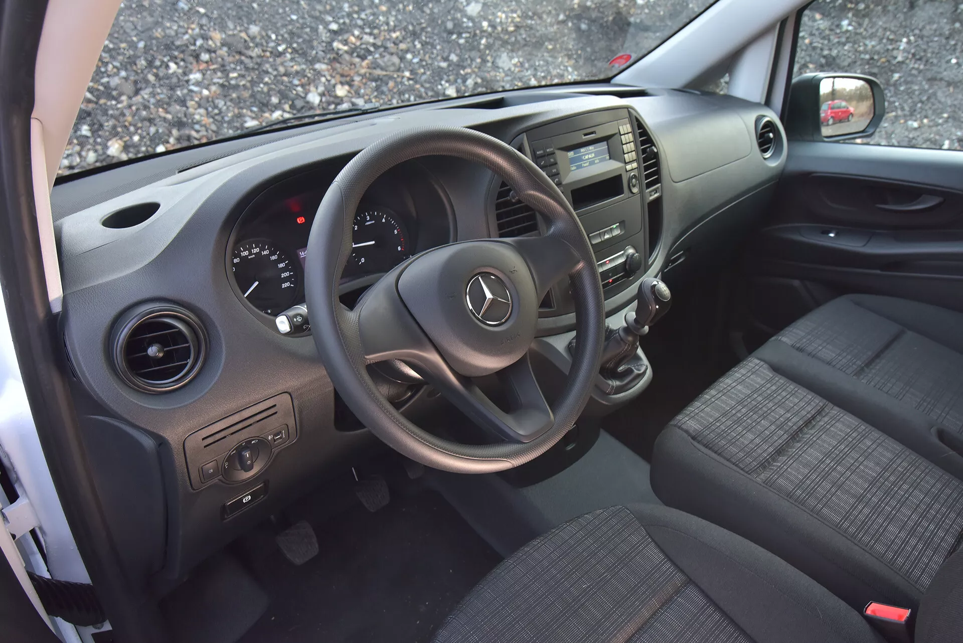 Interiör av Mercedes-Benz Vito Tourer 2014 sedd från öppen förarsida dörr, framhäver ratten med Mercedes-logga, instrumentkluster, mittkonsol, tygsäten, dörrkontroller och luftventiler.