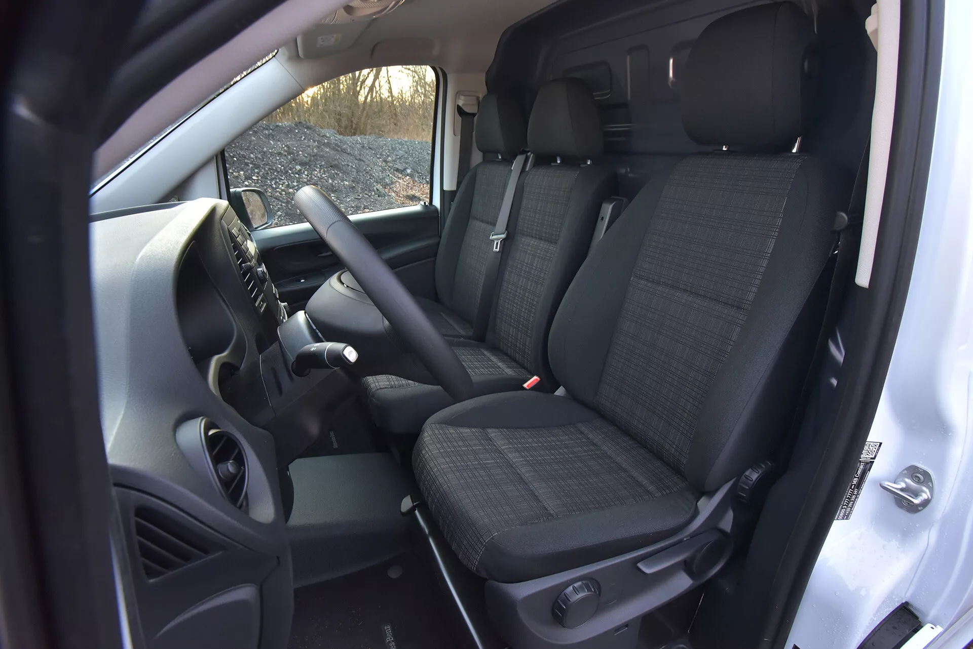 Interiörvy av Mercedes-Benz Vito 2014 (Vito-Tourer) som visar förarens och främre passagerarens område med tekniska funktioner som kontroller på ratten, en central konsol som möjligen innehåller ett infotainmentsystem, framstolar klädda med mönstrat tyg med nackstöd, och en glimt av baksätet, allt taget från ett högt vinkel som framhäver kabinens rymd och manuella transmissionsdetaljer.