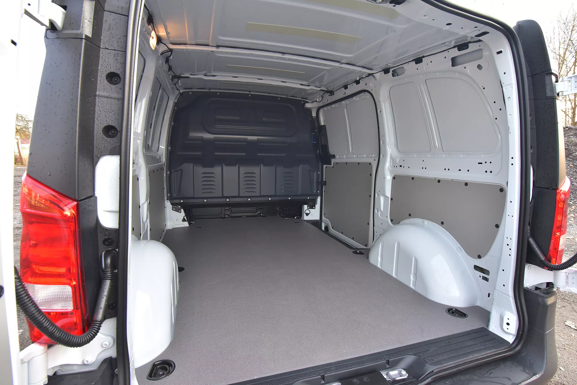 Bakre lastutrymmet i Mercedes-Benz Vito Tourer handelsfordon 2014 med öppna dörrar som visar ett platt slitstarkt golv och en bar metallinteriör för enkel anpassning, sett från ett snett bakre externt perspektiv