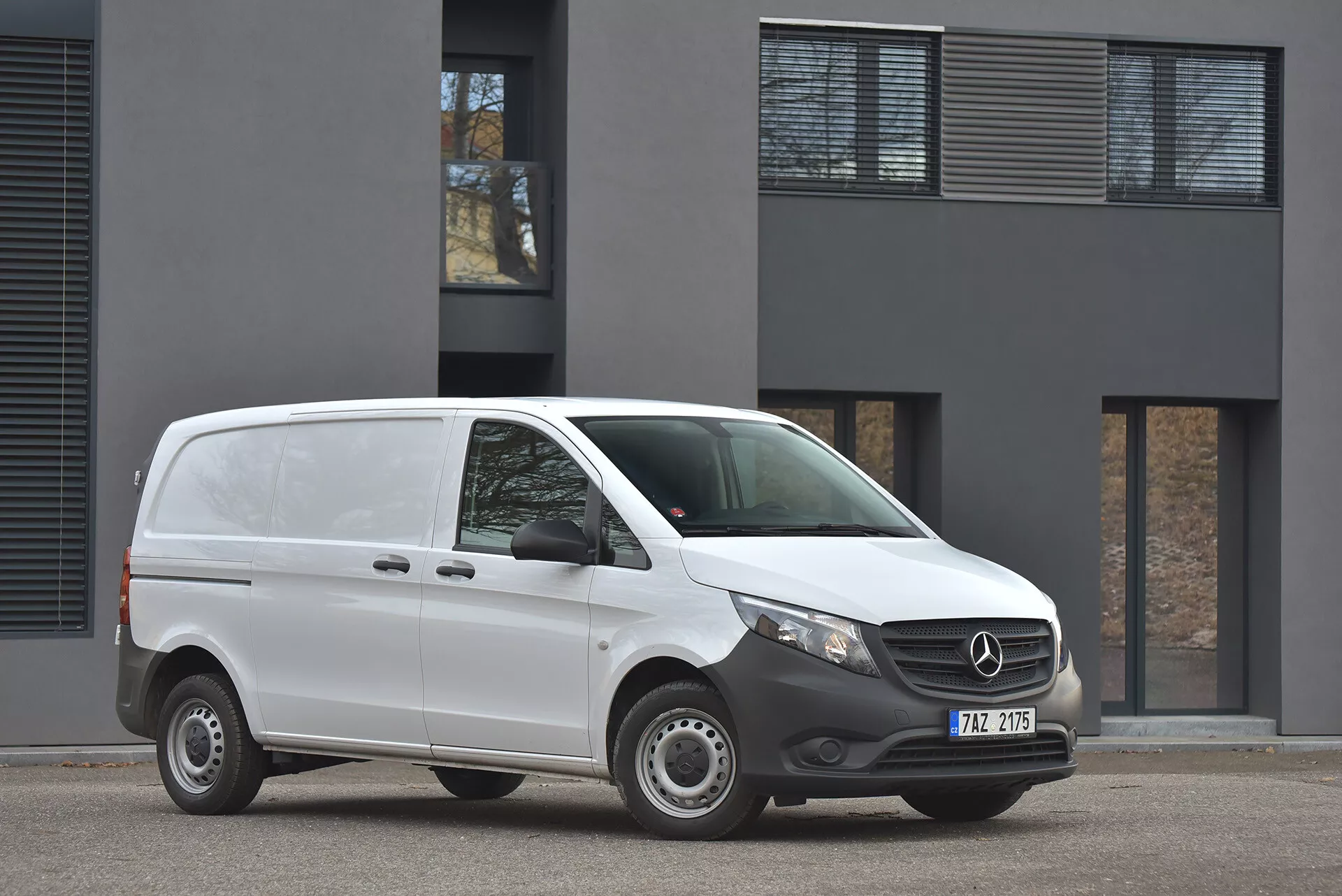 2014 Mercedes-Benz Vito Tourer skåpbil i vitt parkerad på asfalt, visar front- och sidoprofil med tydlig vy av grillmärke och moderna strålkastare, fotograferad i mulen dagsljus framför minimalistisk byggnad