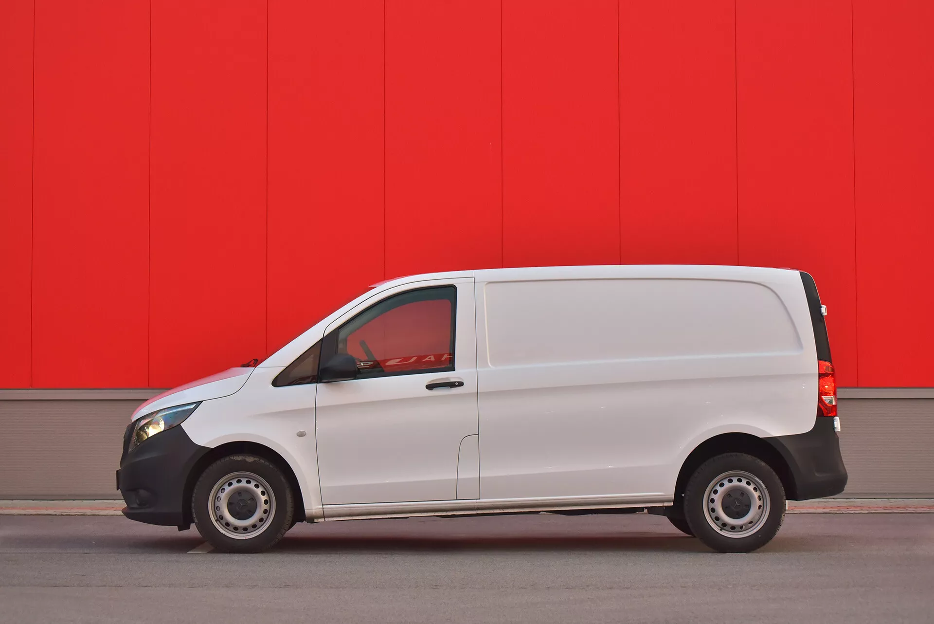 2014 Mercedes-Benz Vito Tourer vit skåpbil parkerad parallellt mot en livligt röd vägg, visar sidoprofil med synlig dörr, fönster och stålhjul fotograferad från ett lågt vinkel för att framhäva fordonets design och egenskaper