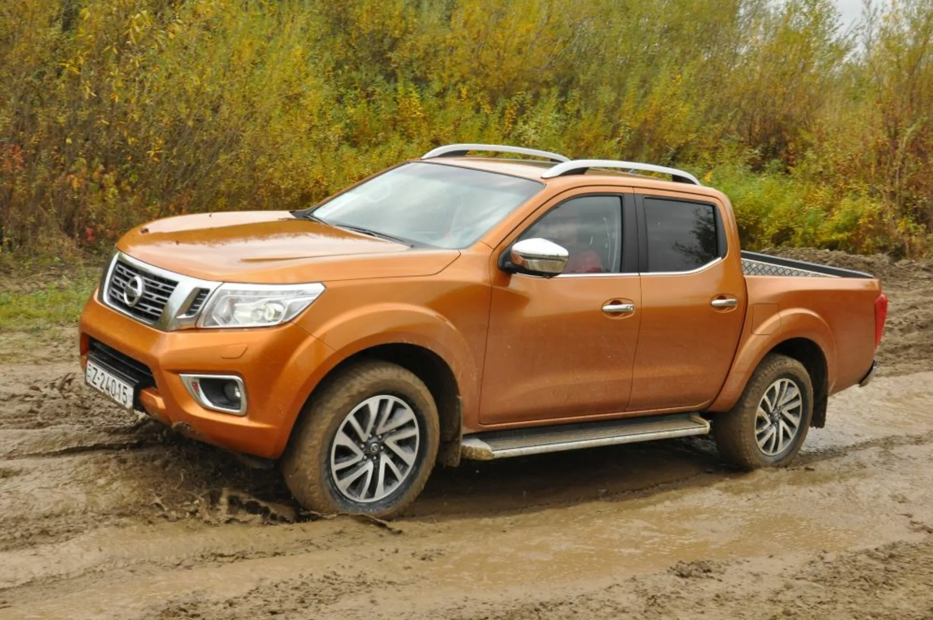 2016 Nissan Navara orange pickup truck i en tre fjärdedels främre vy, som visar strålkastare, kromaccenterad grill, aluminiumsfälgar och besättningskabin konfiguration på grov terräng