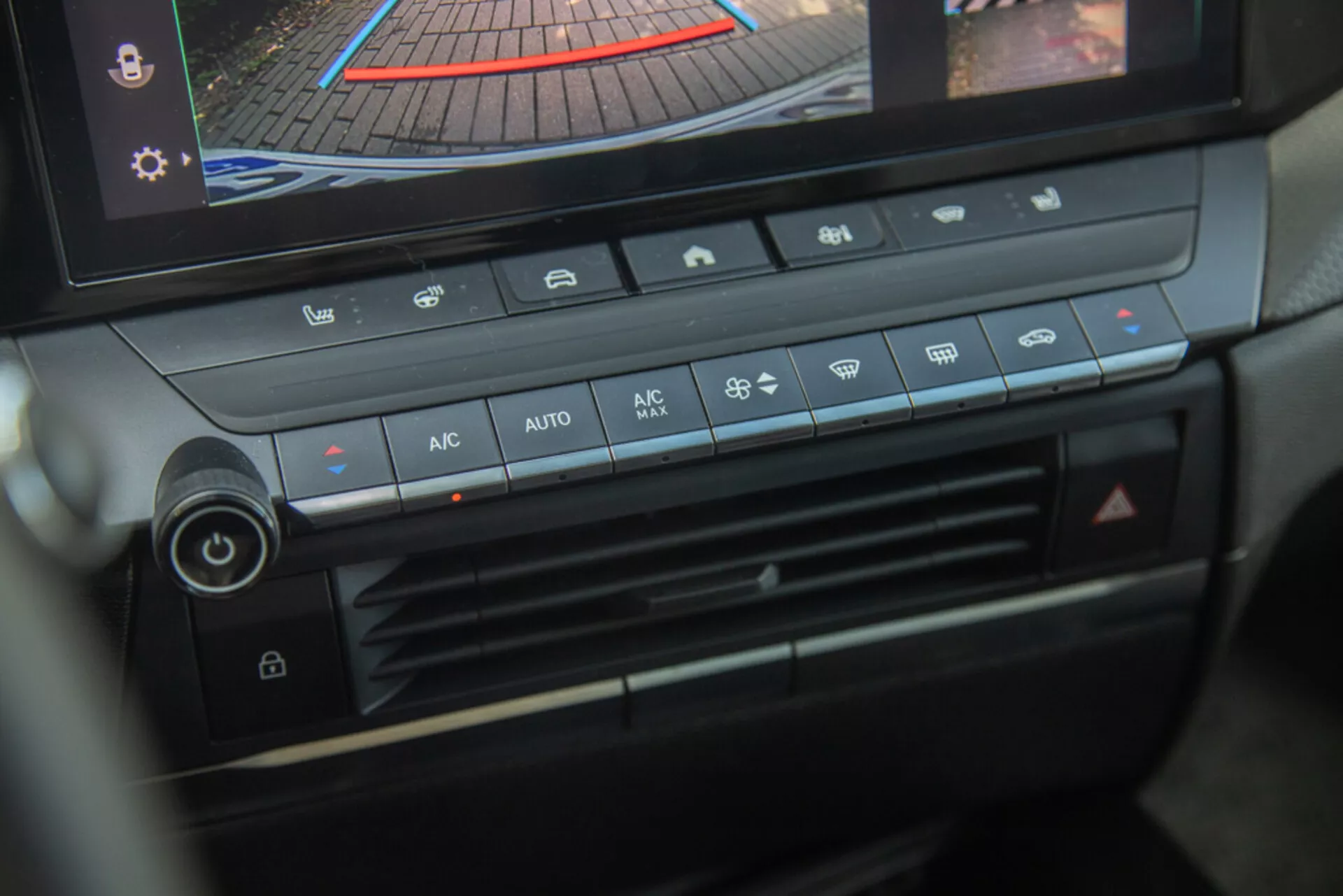 Mittkonsol och klimatkontrollpanel i Opel Astra 2022, med fokus på temperaturjusteringsknopp, fläkthastighet, luftfördelning och knappar för automatisk klimatkontroll med digital display som visar bakåtkamera