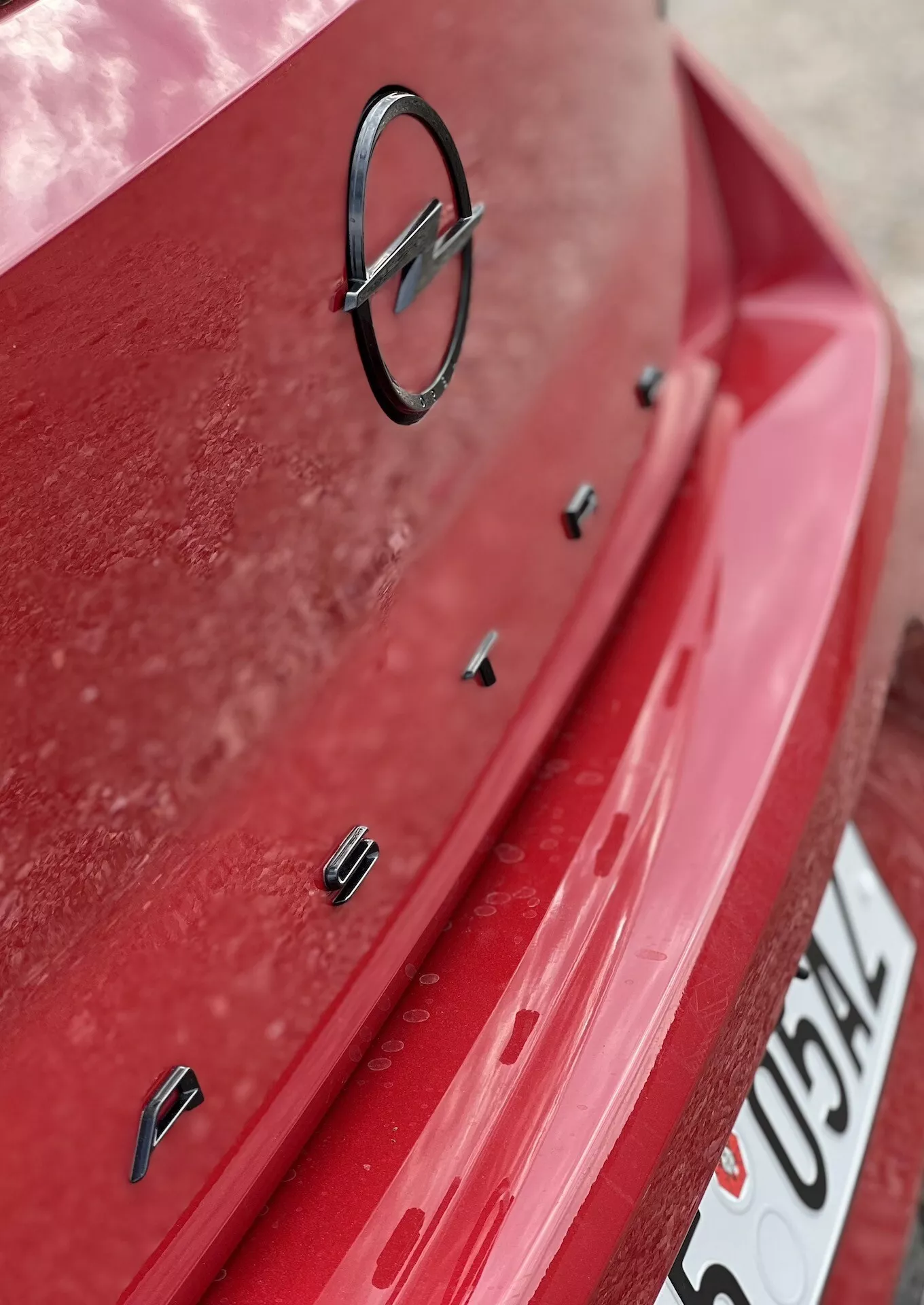 Närbild av baksidan på Opel Astra 2022 med röd lack och synligt dammlager, visar tillverkarens emblem och sensorer för parkeringshjälp