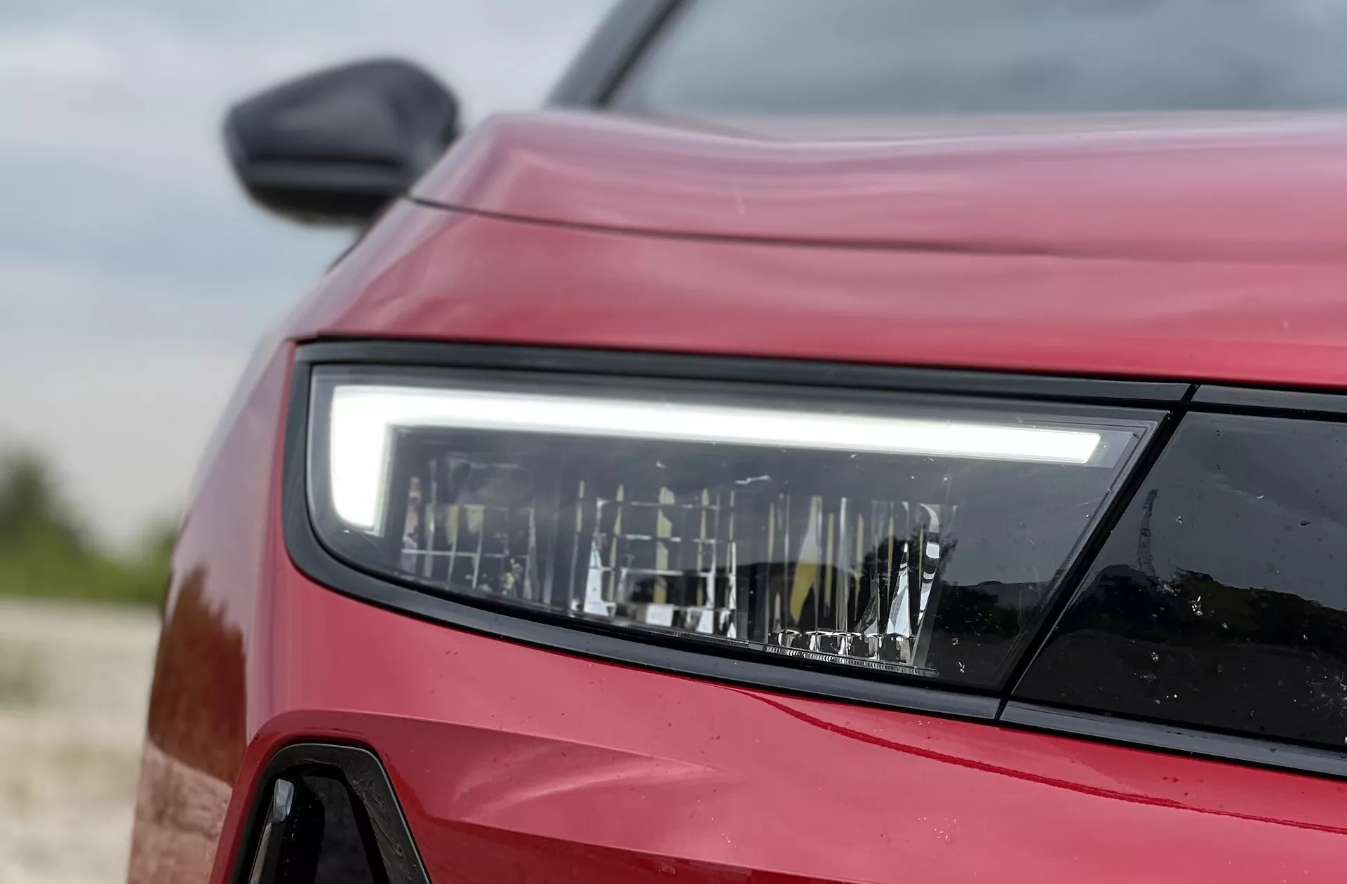 Närbild från sidoframsida av en röd Opel Astra 2022 med fokus på den detaljerade utformningen av LED-strålkastaren, som visar modern belysningsteknik och fordonets konturer