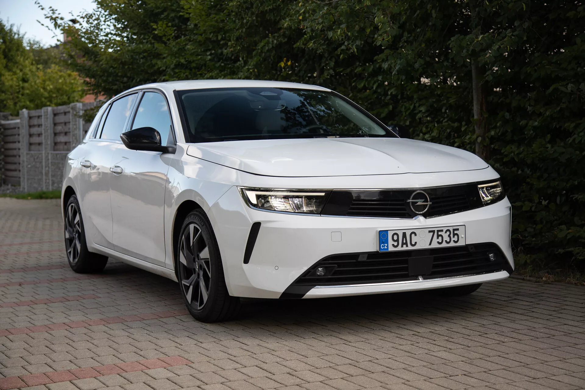 Opel Astra 2022 fångad i en förortsinställning, som visar dess strömlinjeformade strålkastare, framträdande frontgrill, aerodynamisk design inklusive flerspakiga legeringshjul och innovativ teknik från ett tre fjärdedels frontvy