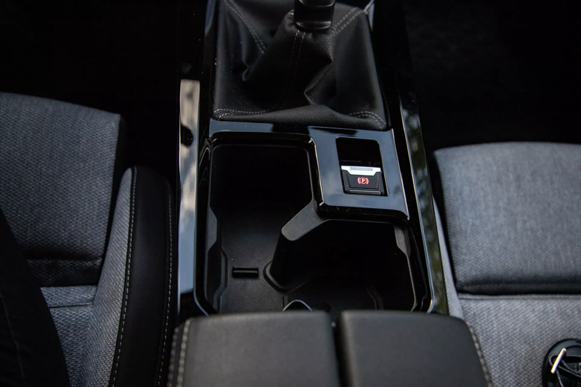 Detaljbild av mittkonsolen i Opel Astra 2022 som visar öppet förvaringsfack, tygklädsel, manuell växelspak med perforerat läder, USB-port och inredningsbelysning