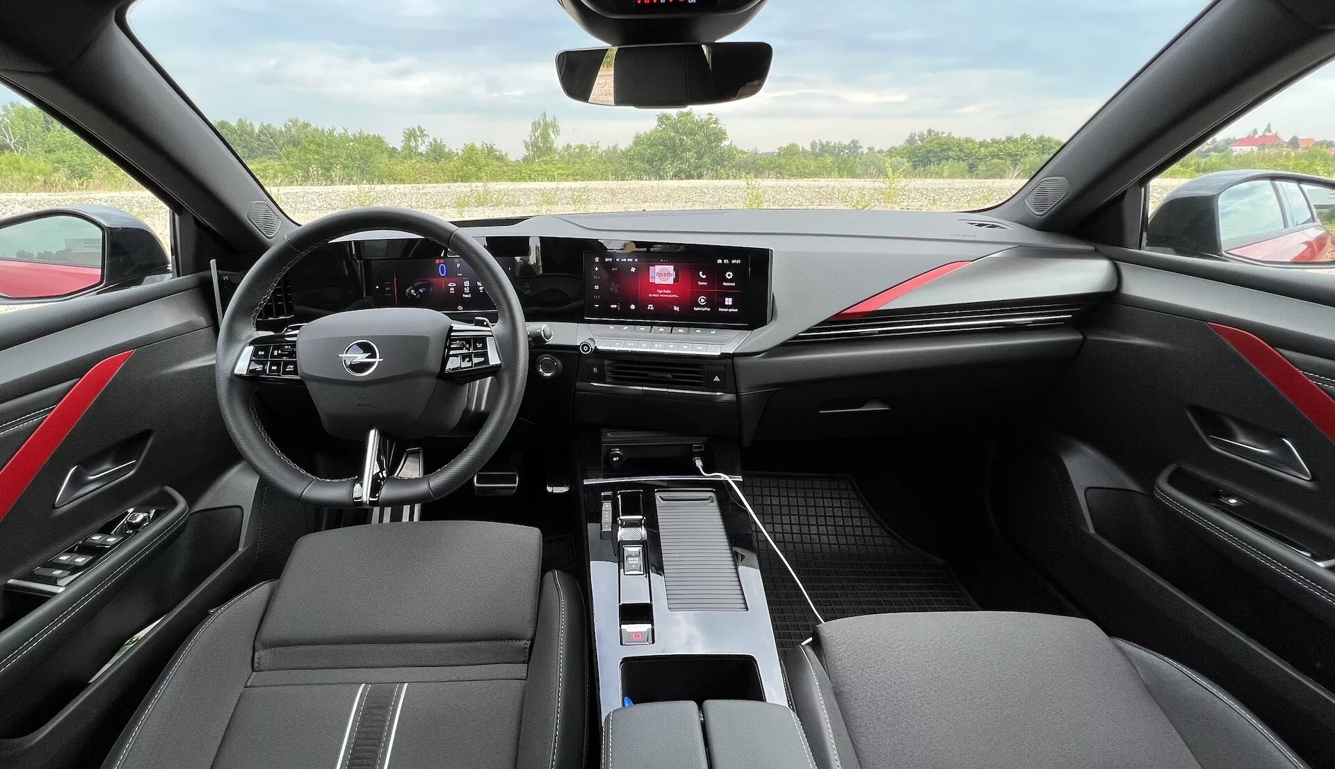 Interiör i Opel Astra 2022 som visar multifunktionellt trespårat styrhjul, digital instrumentpanel, pekskärmsinfotainmentsystem, släta klimatkontroller, tvåtonigt svart läder med röda sömmar och modern kabininredning ur förarens perspektiv