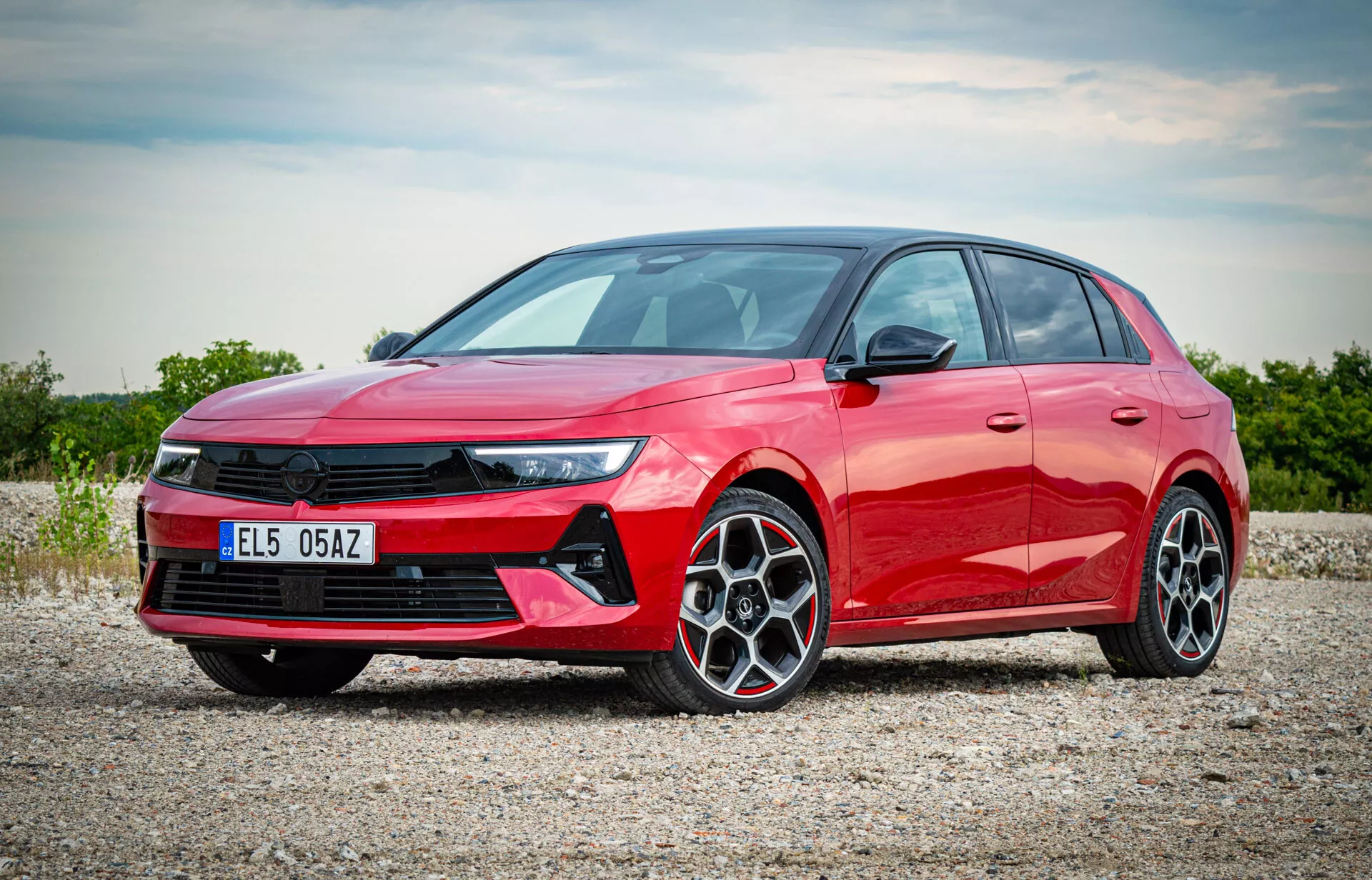 2022 röd Opel Astra hatchback fotograferad från ett trekvarts frontvy visar LED-strålkastarna, framträdande frontgrillen, flerspakiga legeringshjul och den släta sidoprofilen på en grusyta med diffust solljus som belyser bilens moderna funktioner