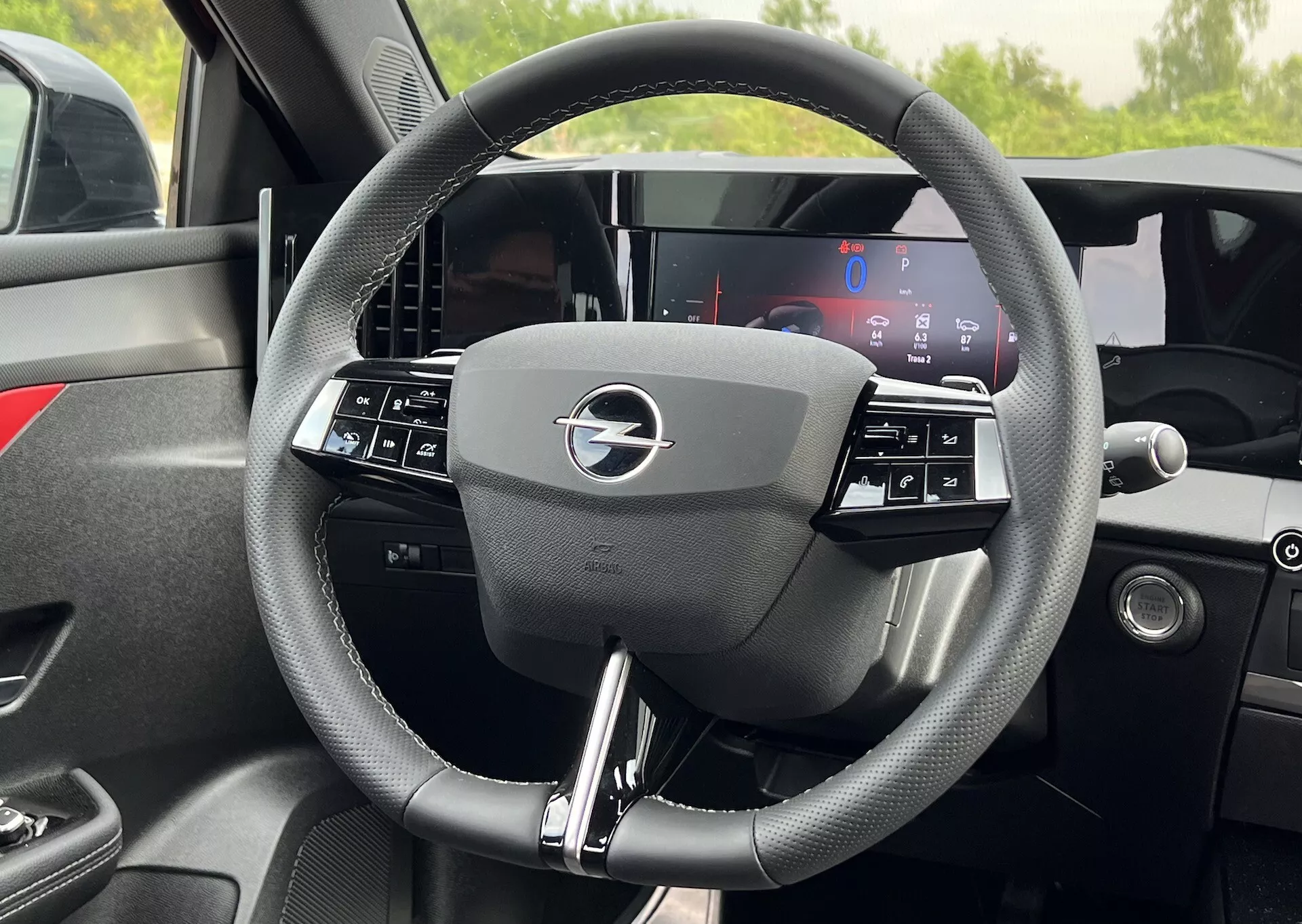 Närbild på interiören av 2022 års Opel Astra ratt med en trespaksdesign med integrerade kontroller och en helt digital instrumentbräda bakom, som belyser modern fordonsteknik och ergonomi
