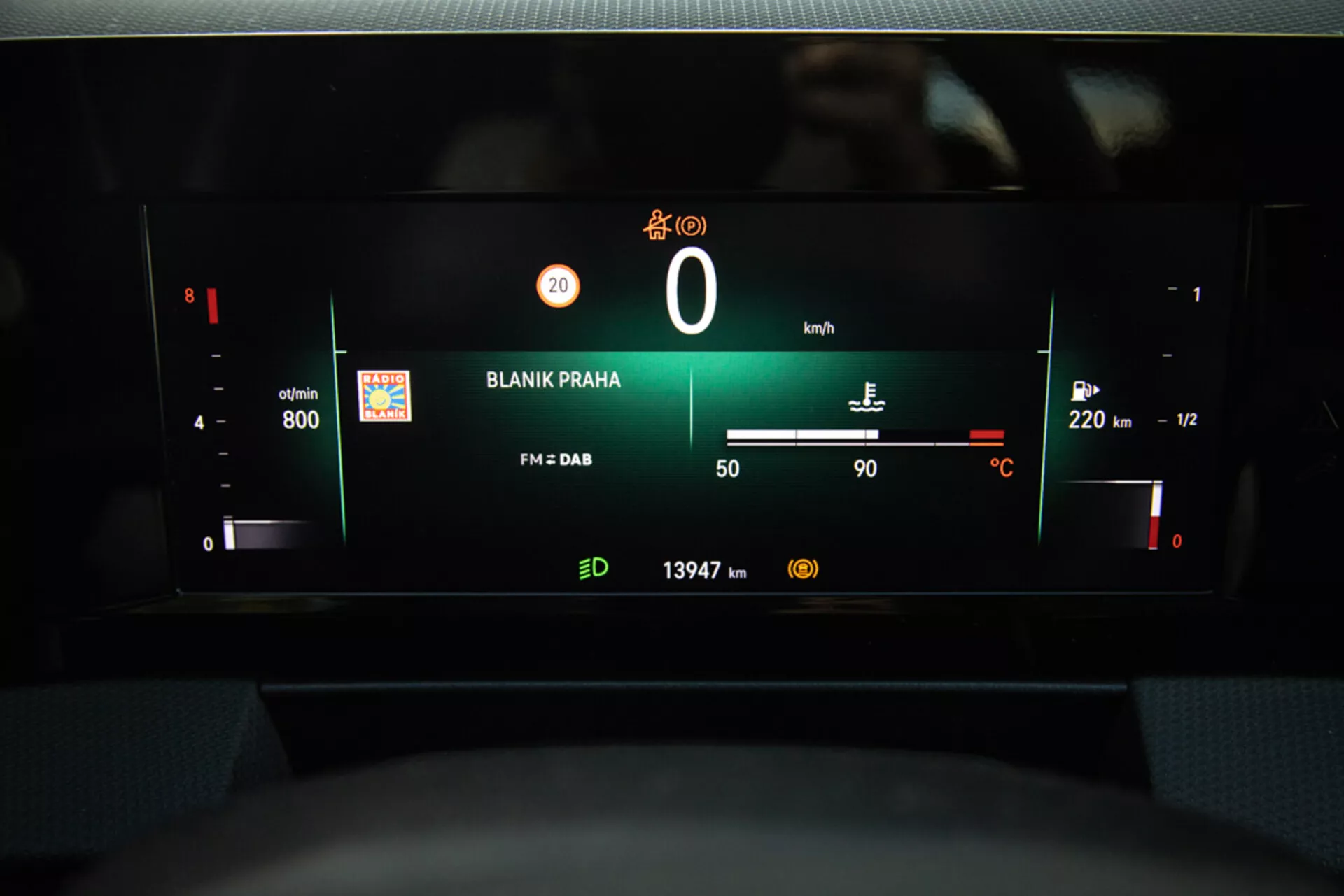 Vy över Opel Astra 2022 digitala instrumentpanel som framhäver instrumentklustret med varvräknare, batterinivå, hastighetsmätare, bränslemätare, utomhustemperatur, radiostation 'BLANIK PRAHA' och mätarställning från förarsätets perspektiv.