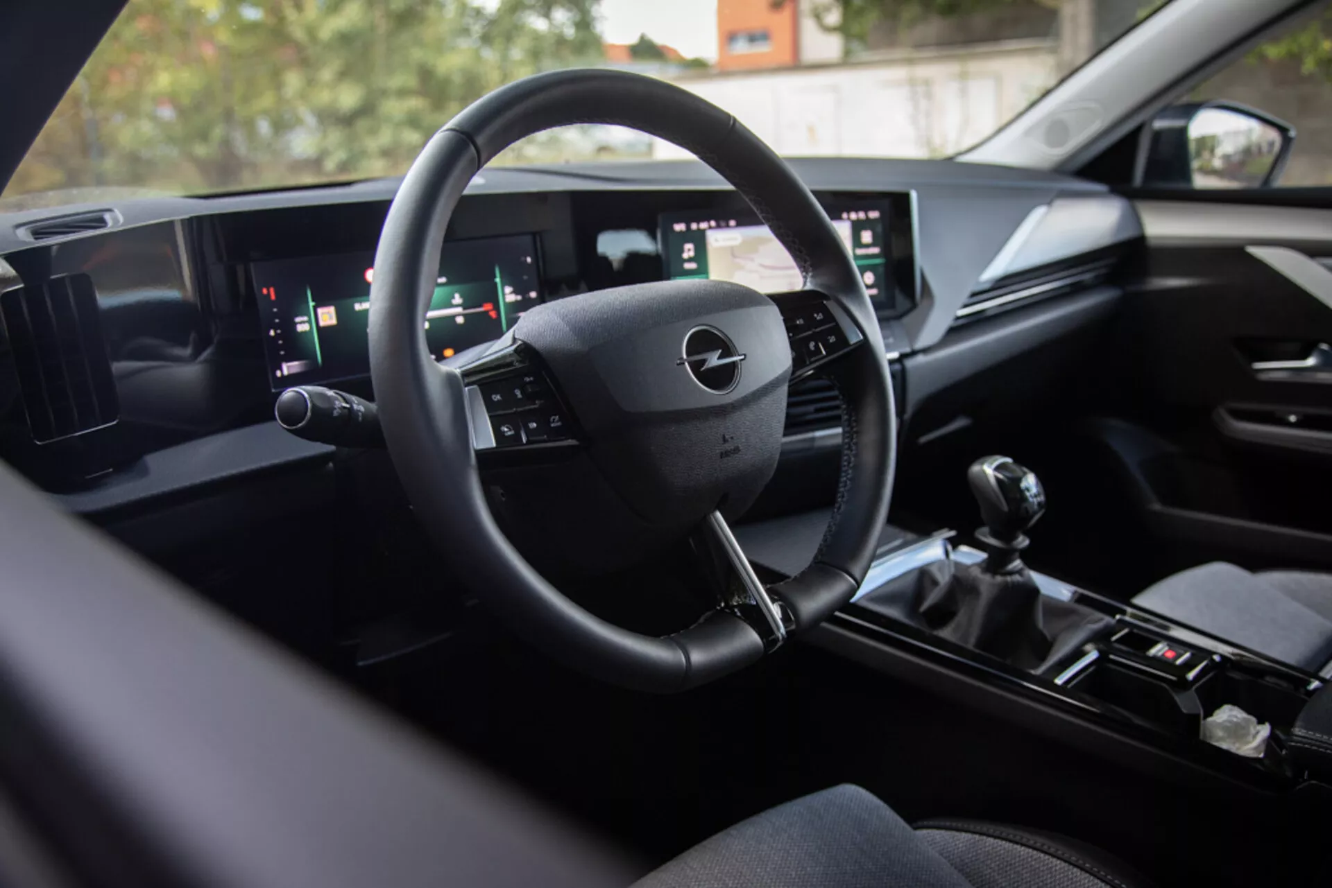 Interiör av Opel Astra 2022 som visar modern digital instrumentbräda teknologi, multifunktionsratt, brett dubbel-skärms infotainmentsystem och manuell växelspak för sportiga prestanda, sett från baksätet mot förarområdet med premium avslutningar