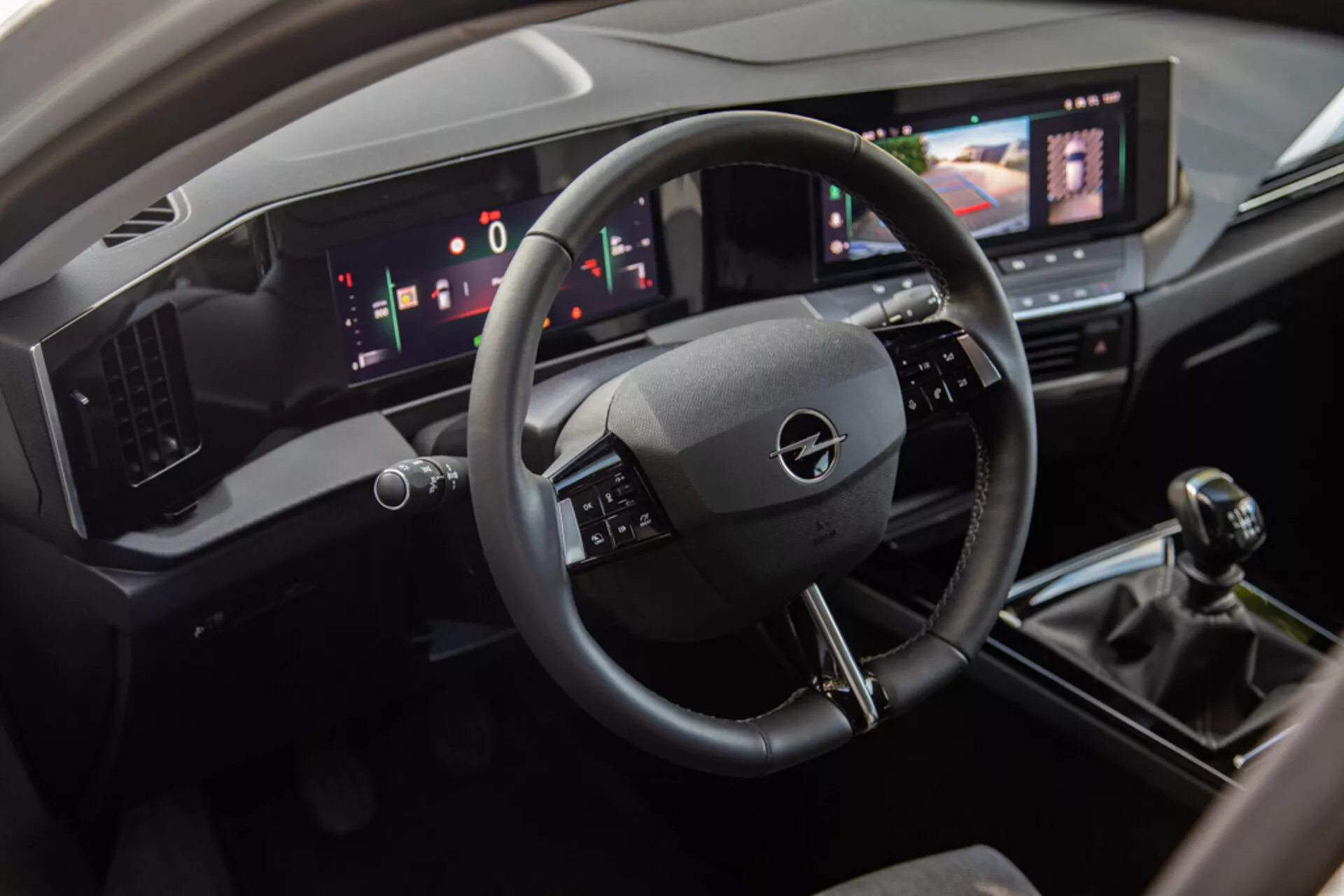 Interiörvy av Opel Astra 2022 som visar förarens område med ett trespoke ratt, digital instrumentpanel och mittkonsol inklusive en pekskärm för infotainment system, manuell växelspak och moderna klimatkontroller