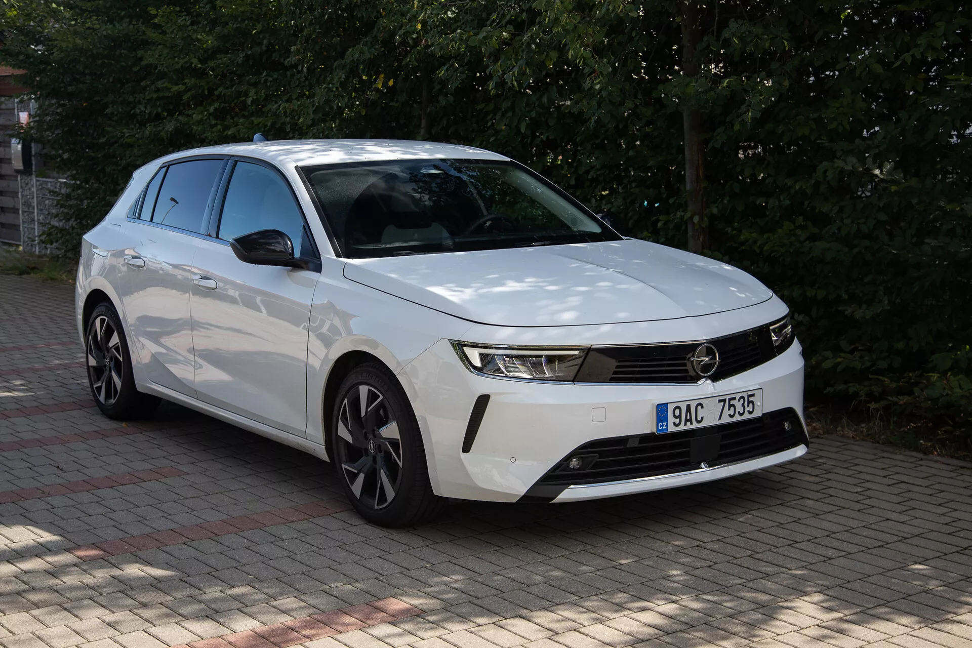 Vit Opel Astra 2022 med distinkt frontdesign, slanka strålkastare, horisontell grill, aerodynamisk stötfångare, konturerad motorhuv och flerspakiga lättmetallfälgar fångad från ett tre fjärdedels främre perspektiv utomhus under dagen