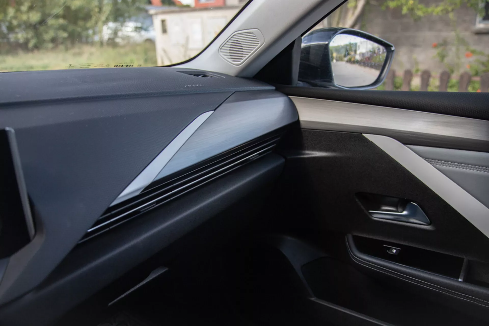 Interiörvy från passagerarsätets perspektiv som visar instrumentbrädans design, inredning, och dörrpanel i en Opel Astra 2022, med mörka, snyggt konturerade linjer med fokus på materialtextur och eventuella teknologiska integrationer