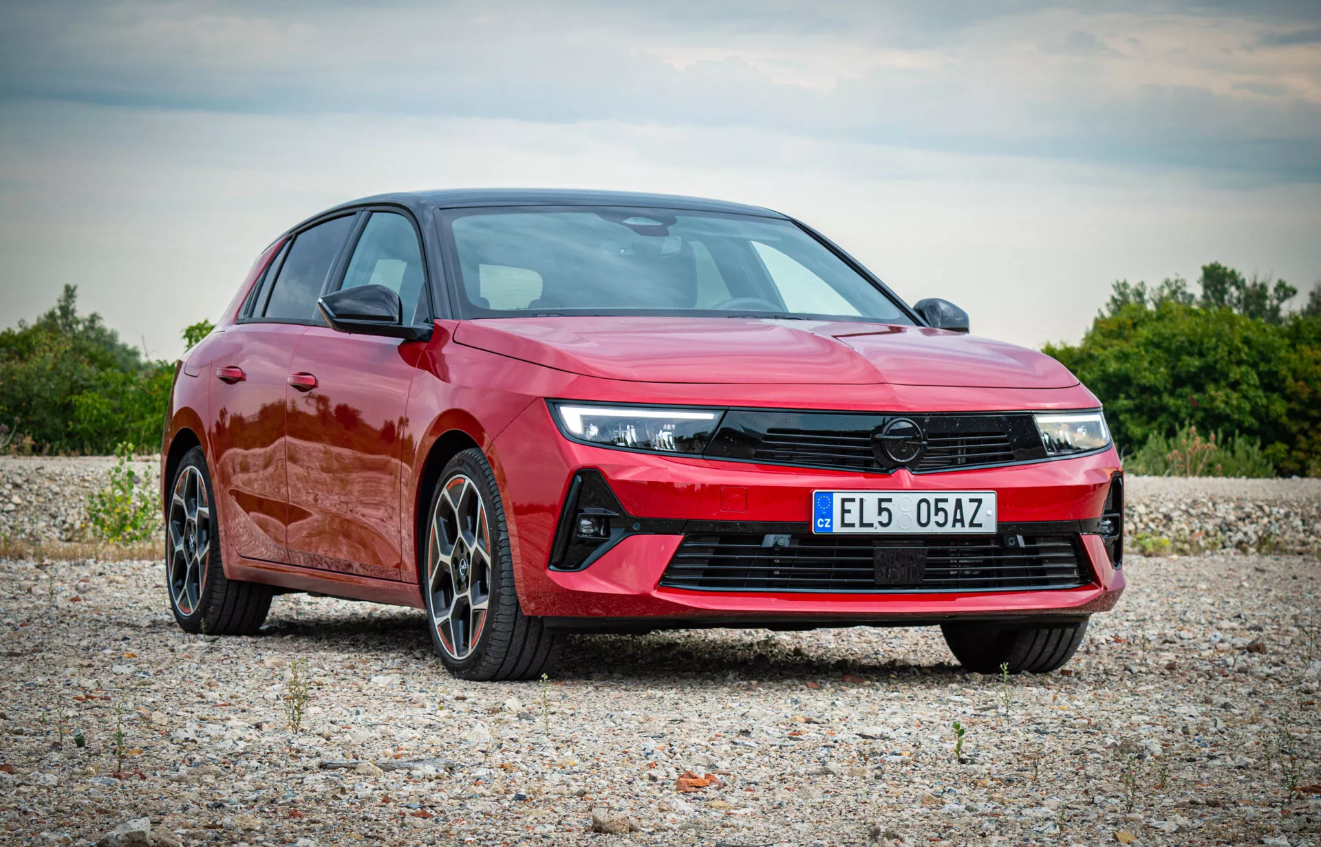 Opel Astra 2022 i livlig röd, visar modern design med vinklade LED-strålkastare, framträdande frontgrill, sportig frontstötfångare och flerspakiga legeringshjul, visas i en naturlig utomhusmiljö från en tre fjärdedels framifrån vy som framhäver bilens aerodynamiska profil och premiumfunktioner
