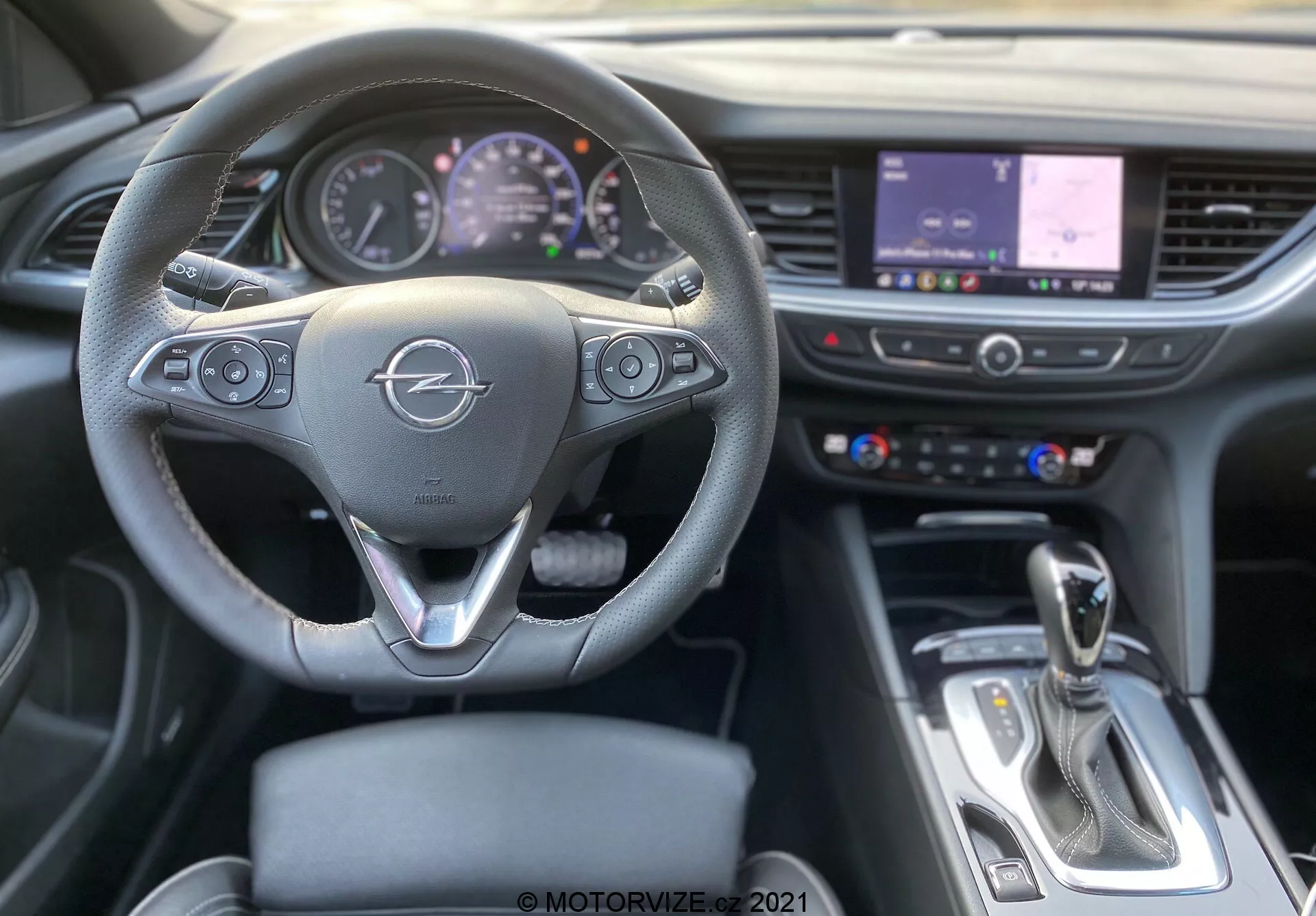 Interiörbild av en Opel Insignia GSI Grand Sport 2020 från förarsätets perspektiv, med fokus på den treekrade ratten med multimediaknappar och fordonskontroller, analogt och digitalt instrumentkluster, central infotainment pekskärm som visar en karta, växelspak, kromdetaljer och en modern blandning av material som läder och metall.