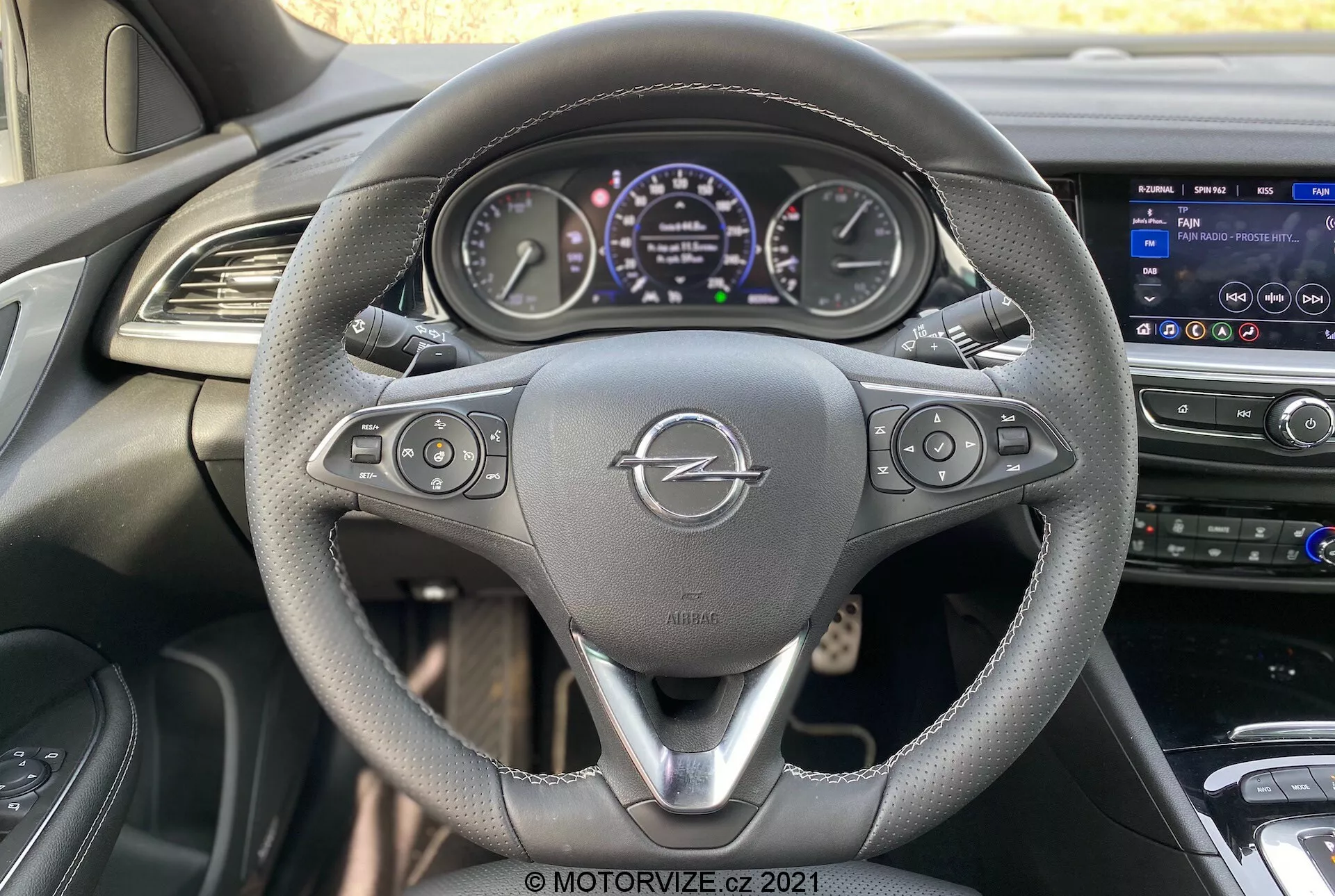 Interiörperspektiv av 2020 Opel Insignia GSi Grand Sport från förarsätet, med en treekrad läderratt med kontrollknappar, en digital instrumentpanel som visar mätare och fordonsinformation, och en mittkonsol med ett infotainmentsystem med pekskärm och ventilationsuttag för klimatkontroll.
