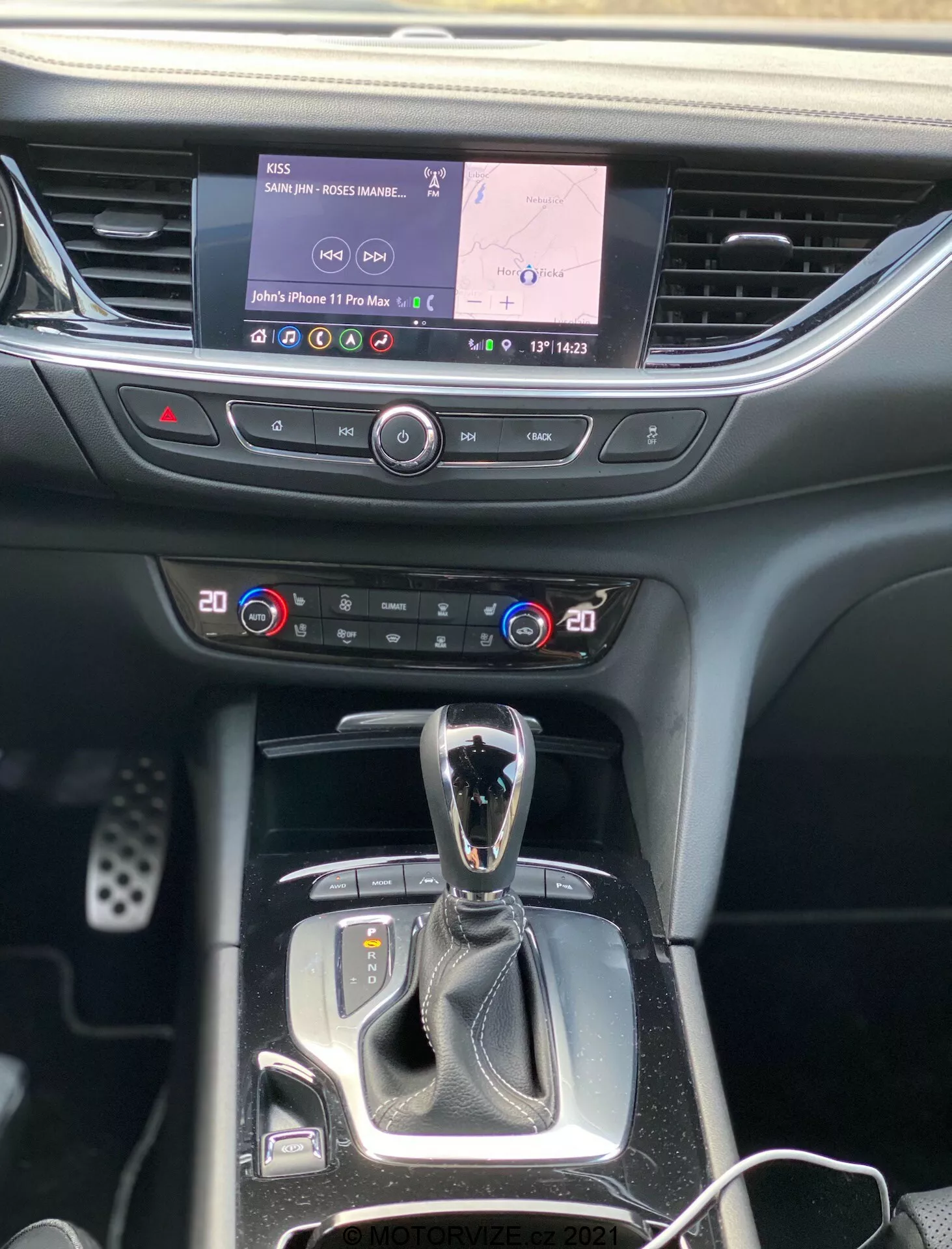 Interiörvy av Opel Insignia 2020 fokus på den centrala konsolen och instrumentbrädan, visar infotainment-skärmen med navigation och multimedia, tvåzons klimatanläggning, automatisk växelspak med körlägesväljare och knappar för olika funktioner, allt inramat i en blandning av mjuk plast och dekorativa material.