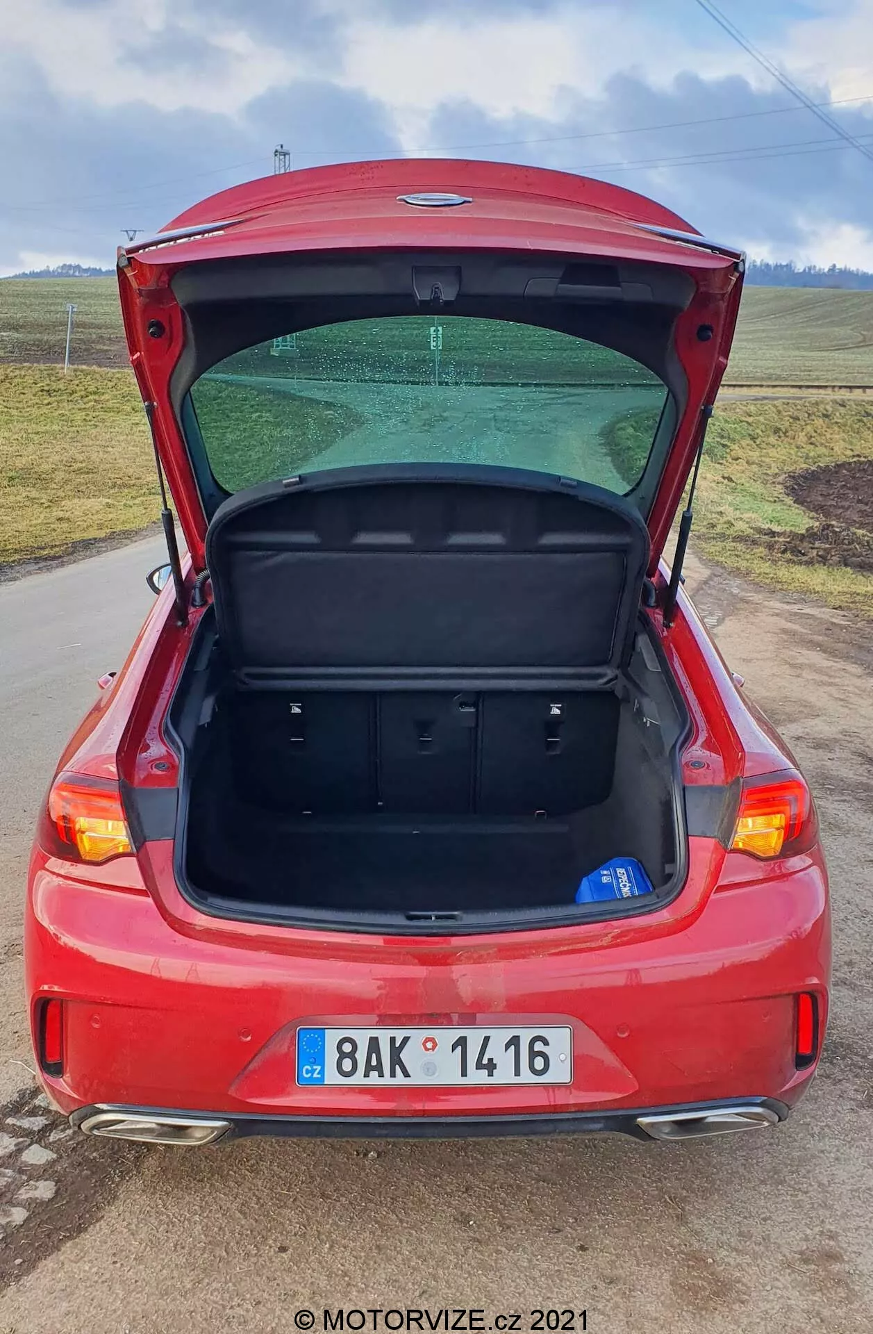 Bakre perspektivet av en röd 2020 Opel Insignia GSi Grand Sport hatchback med sin baklucka upplyft, vilket visar bagageutrymmet inuti. Bilden framhäver fordonets baklyktor, bakre stötfångare, registreringsskylt, bakruta och vindrutetorkare. Fotografens förhöjda vinkel ger en omfattande vy över bilens bakre designelement från nära håll, vilket betonar rymligheten och användbarheten hos hatchback-designen.