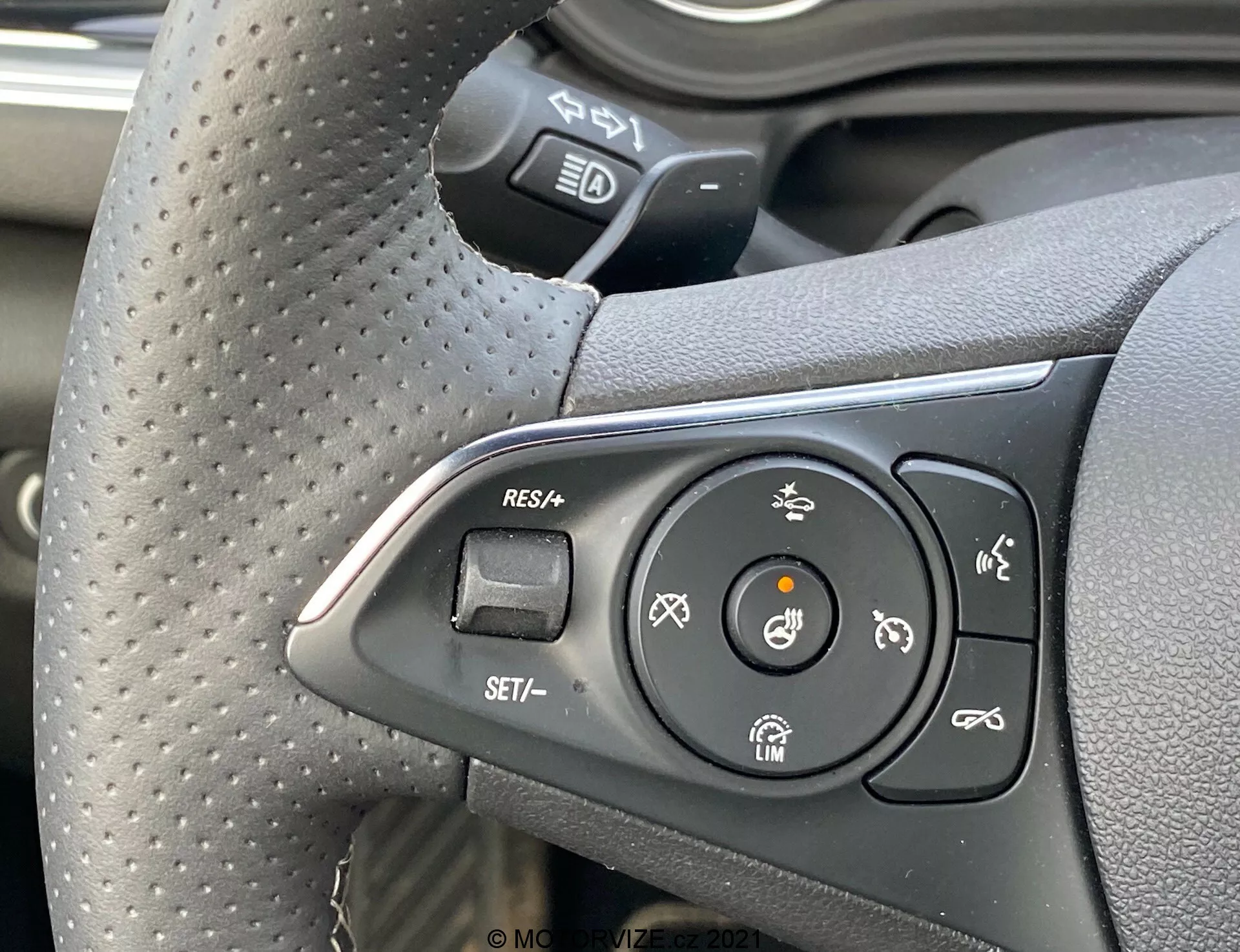 Närbild av den vänstra kontrollgruppen på ratten i en Opel Insignia GSi Grand Sport 2020 från förarens perspektiv, med knappar för farthållare, uppvärmd ratt och filhållningsassistans, med ett texturerat grepp som indikerar komfort och sportighet.