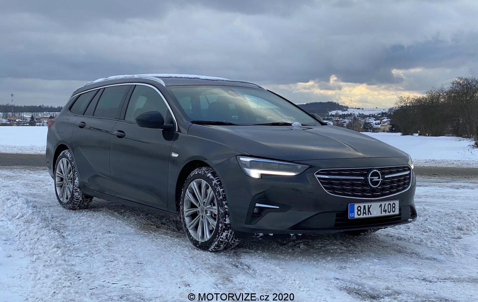 Bild av en modern Opel Insignia Sports Tourer 2020 kombi i en vintrig miljö med snö, molnig himmel i bakgrunden, som visar dess främre grill, eleganta LED-strålkastare, skulpterad motorhuv, takräckessystem, sidohöjd med krominramning, flerspokedaluminiumfälgar med vinterdäck och allmänt vintervägskick.