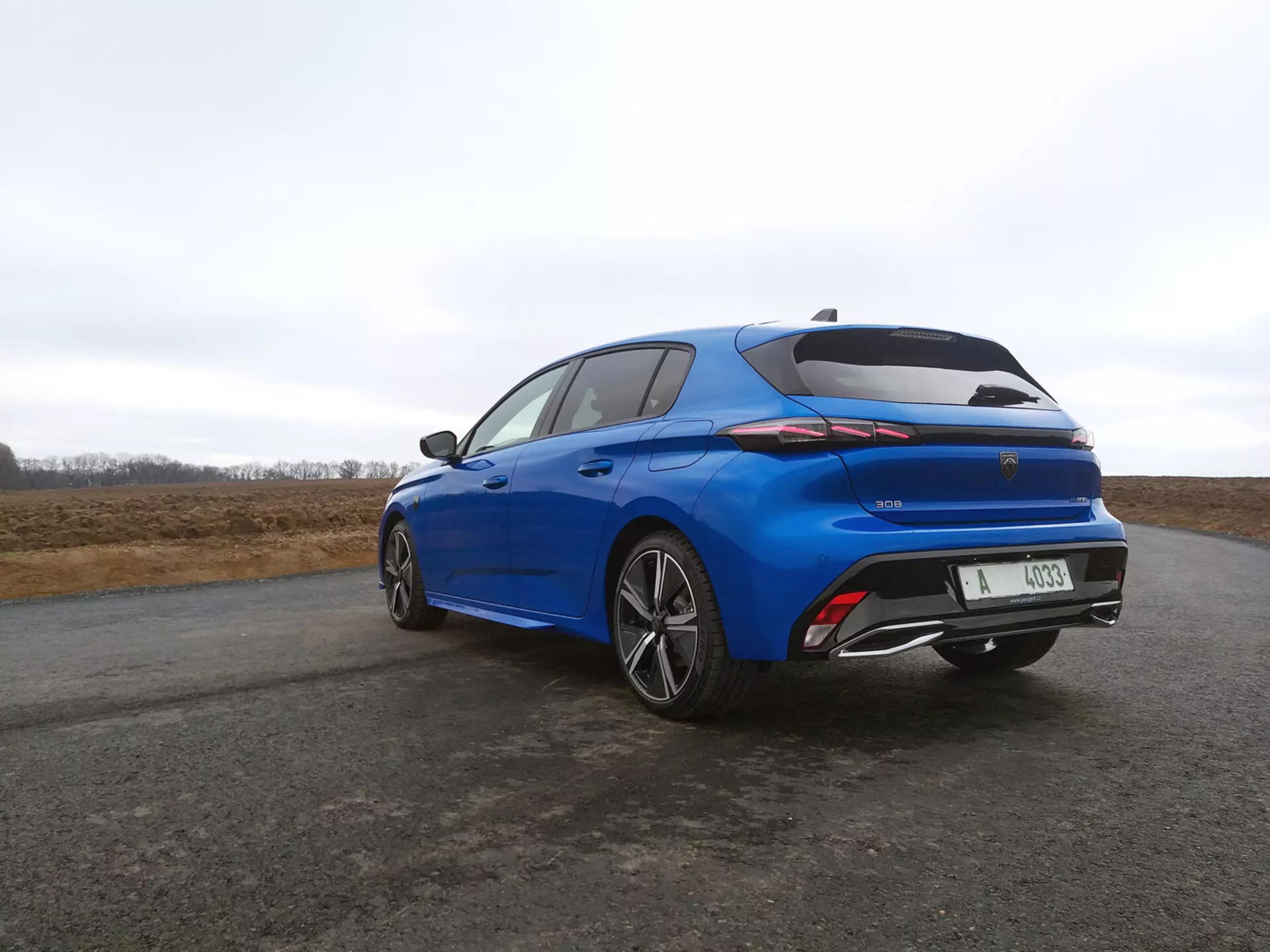 Peugeot 308 hatchback 2022 i strålande blått, bakre tre fjärdedels vy som visar LED-bakljus, integrerad spoiler och flerspakiga aluminiumhjul mot en molnig himmel.