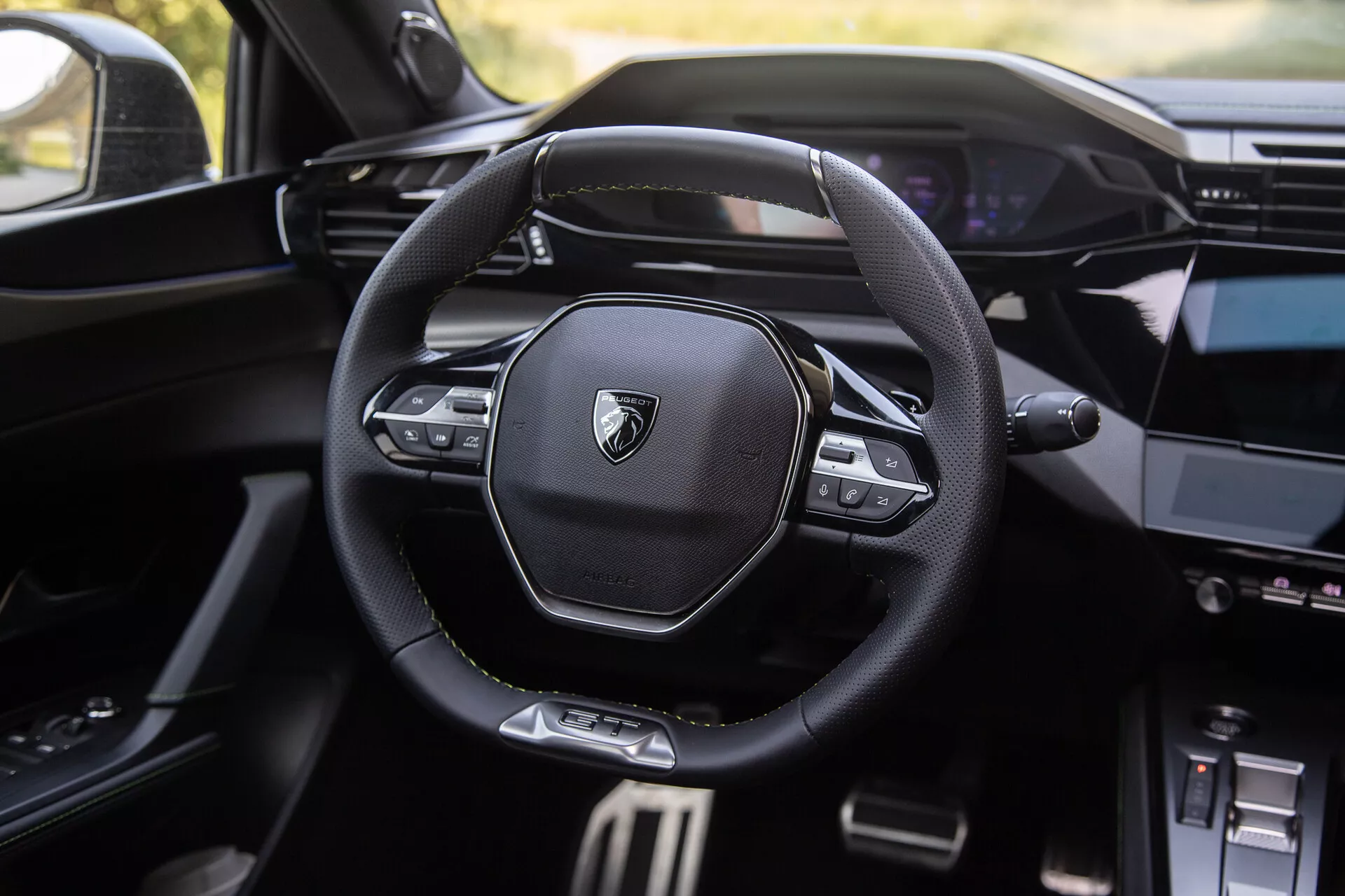 Interiör av Peugeot 408 2023 som visar en modern multifunktionell ratt med varumärkeslogga, digital instrumentbräda i bakgrunden och delvis synlig mittkonsol med infotainmentsystem